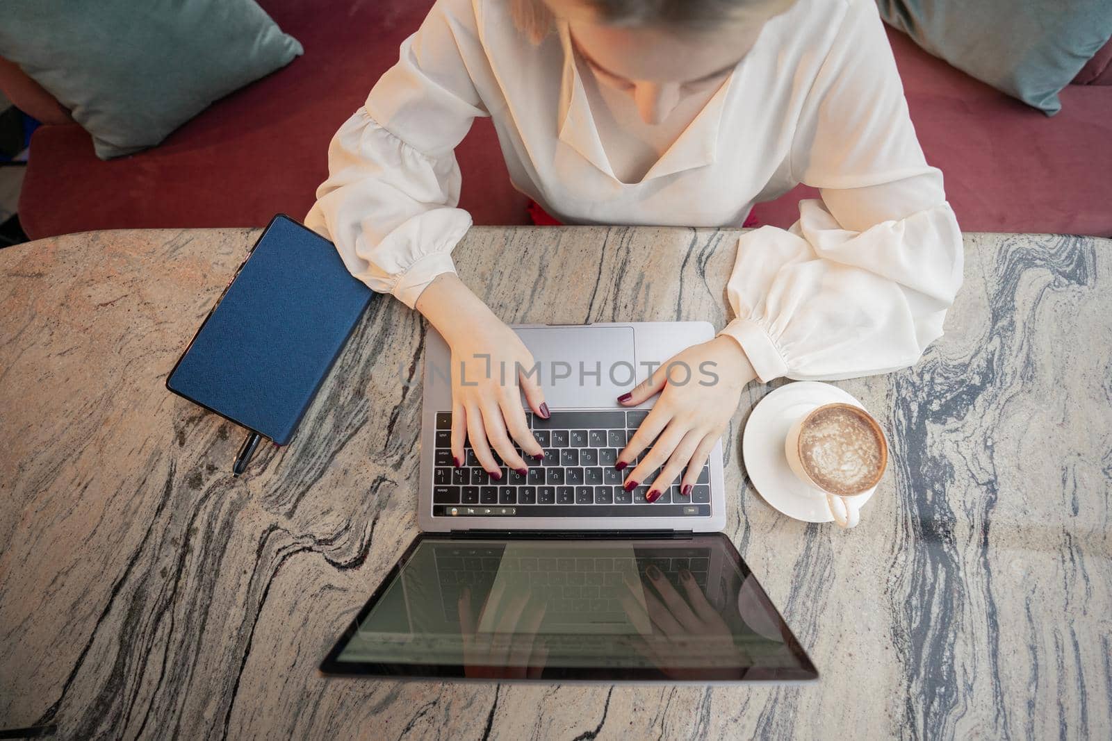 A young attractive business woman sitting in a cafe with a laptop and coffee by Mariakray