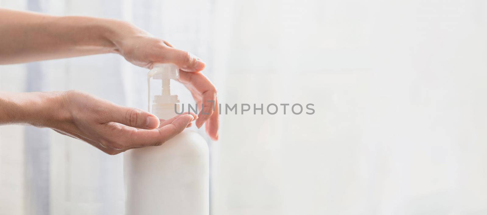Woman hands pushing pump plastic soap bottle on white background with copy space by Mariakray