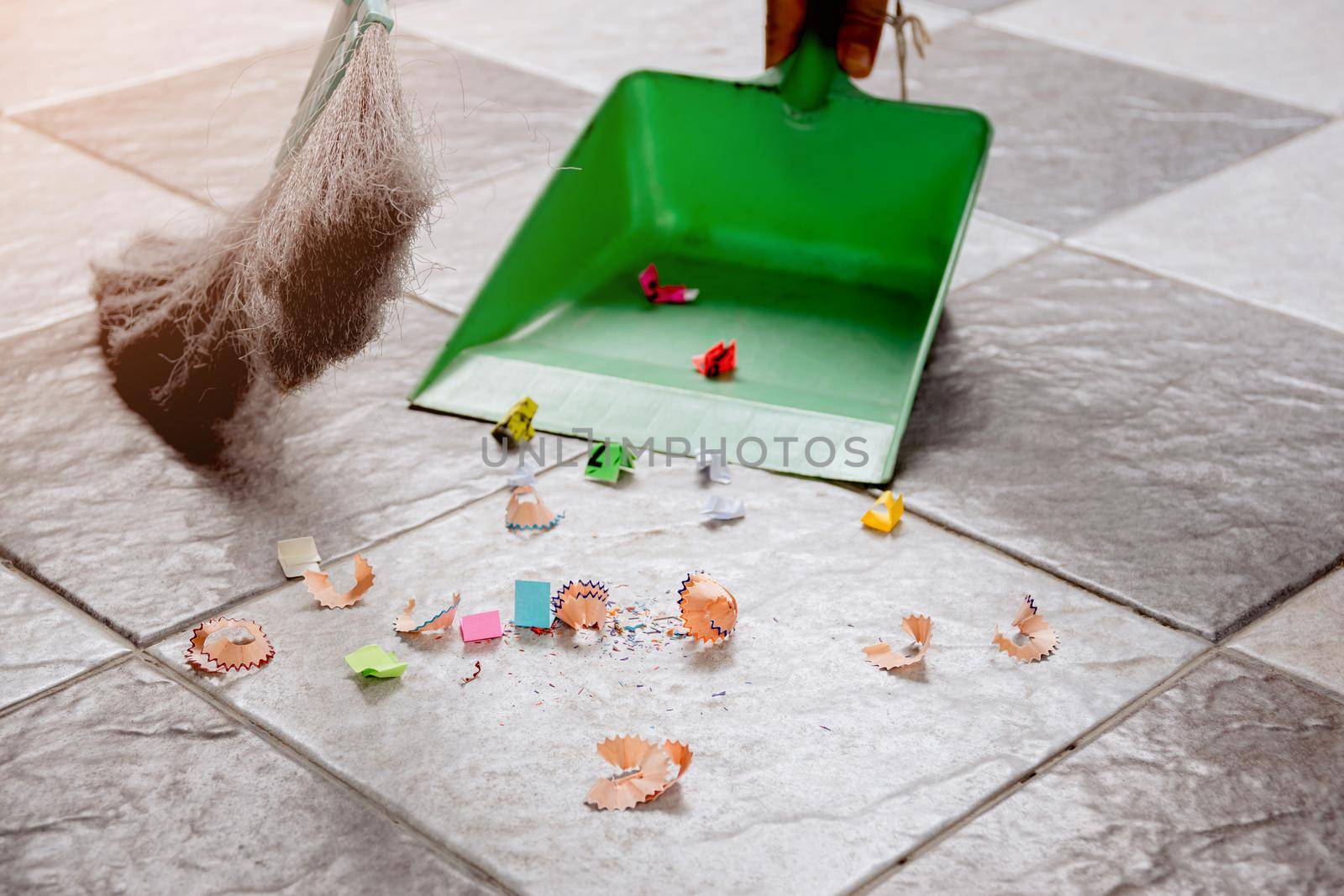 Sweep up scraps of paper and dust on tile floors with a broom and a plastic dustpan. by wattanaphob