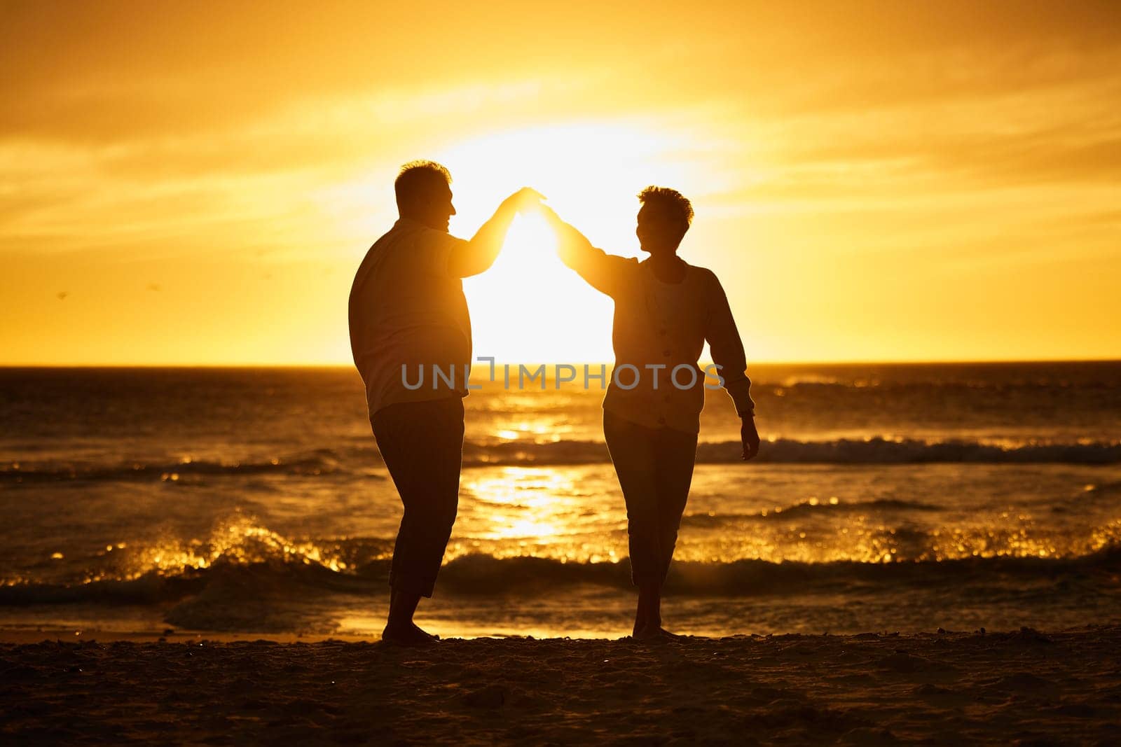 Love, ocean and sunset, silhouette of couple on beach holding hands in Bali. Waves, romance and man and woman dancing in evening sun on romantic vacation spending time together in nature and sea sand by YuriArcurs