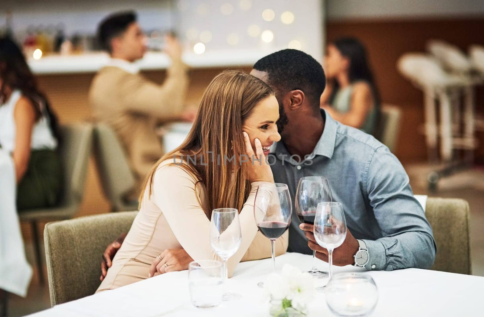 Love, man whisper with woman and in restaurant with wine glasses, happiness or cheerful on Valentines day. Romance, couple or flirty for quality time, romantic or conversation with fine dining or joy by YuriArcurs