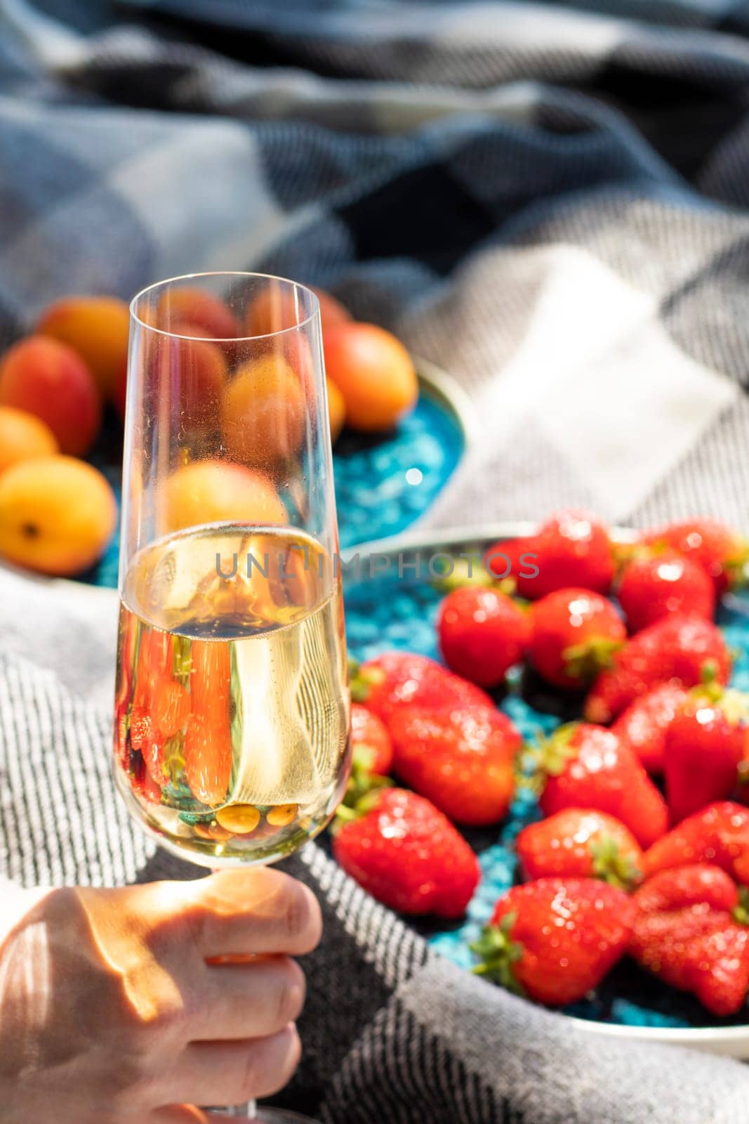 strawberries on plate with glass of champagne or white wine on picnic. Luxury lifestyle, travel concept. glass raised in hand for toast. Ripe berries. wine tasting. Vineyard. Summer fruits. aesthetics