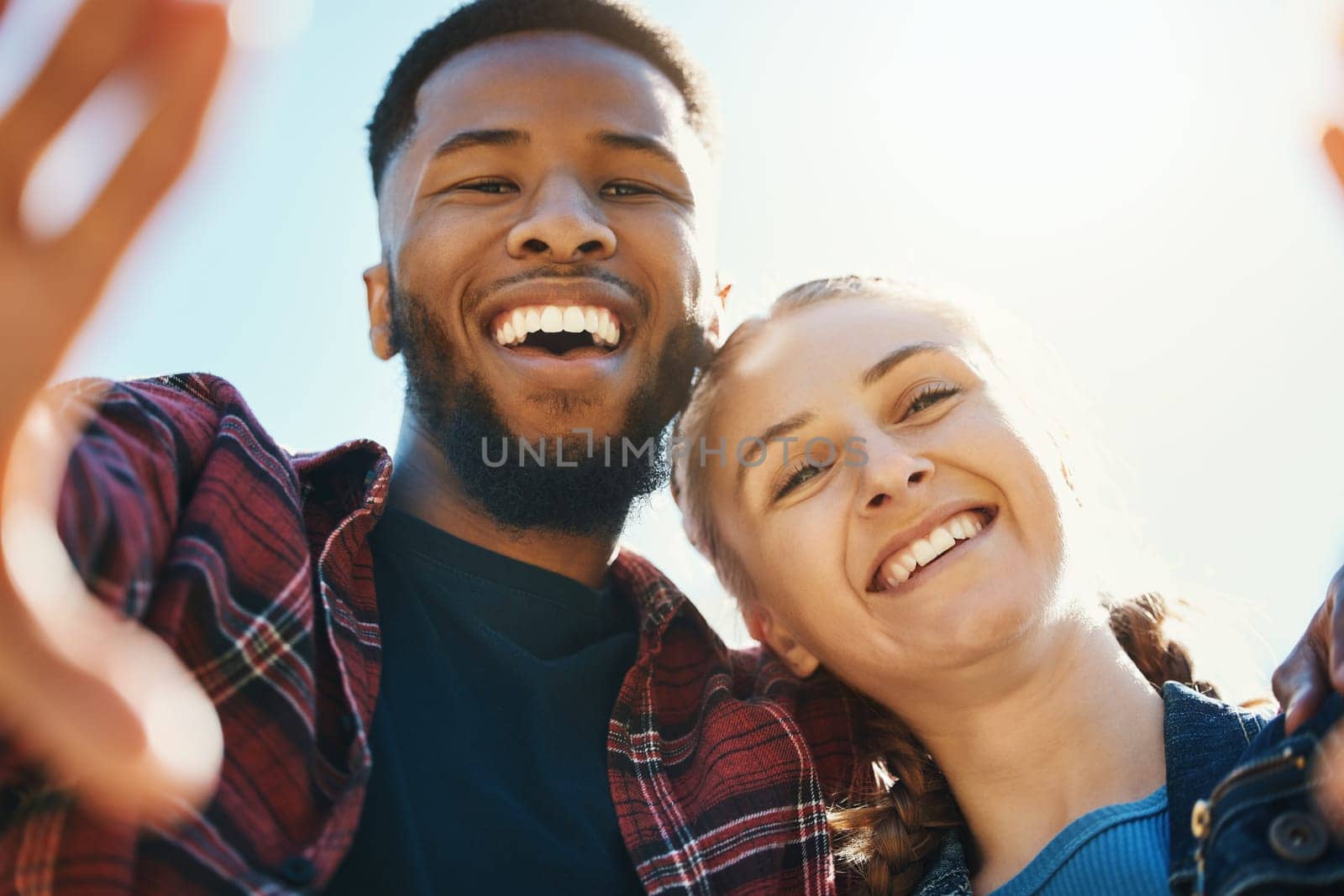 Interracial love, couple selfie and laughing at funny joke outdoors, having fun or bonding in low angle. Comic smile, romance portrait and black man and woman take pictures for happy memory together by YuriArcurs