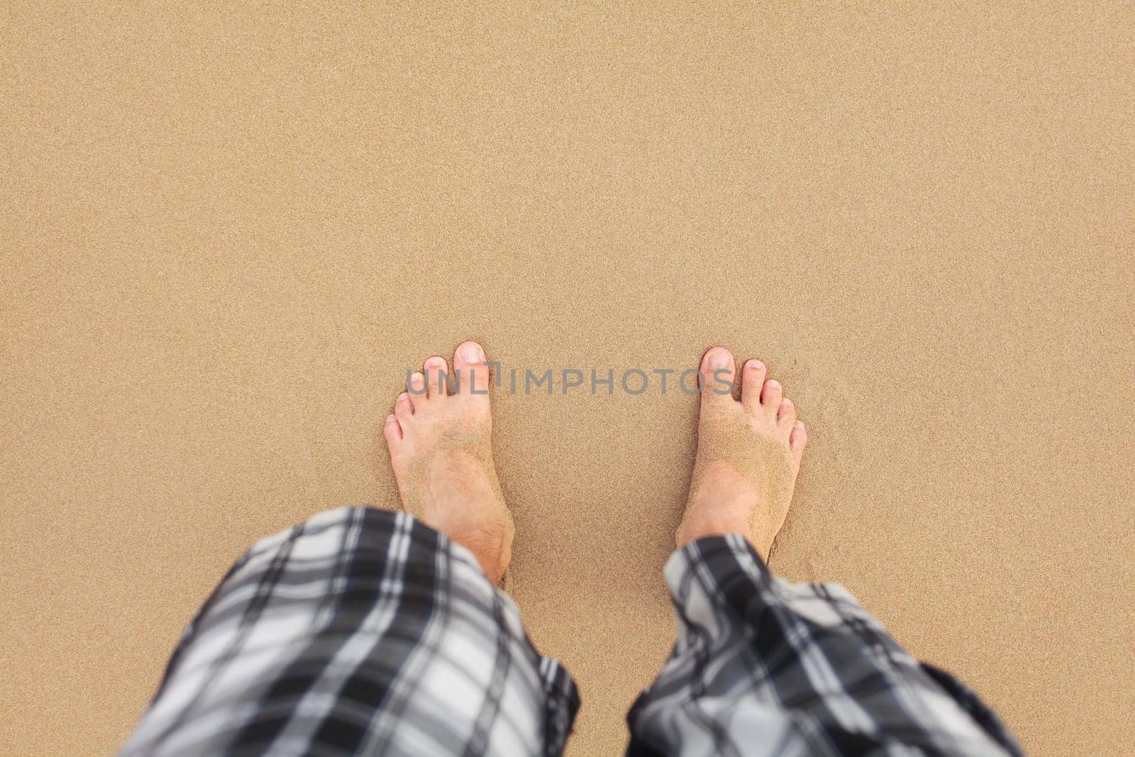 Top down view, man wearing black and white shorts feet in wet sand on beach. Space for text upper part.