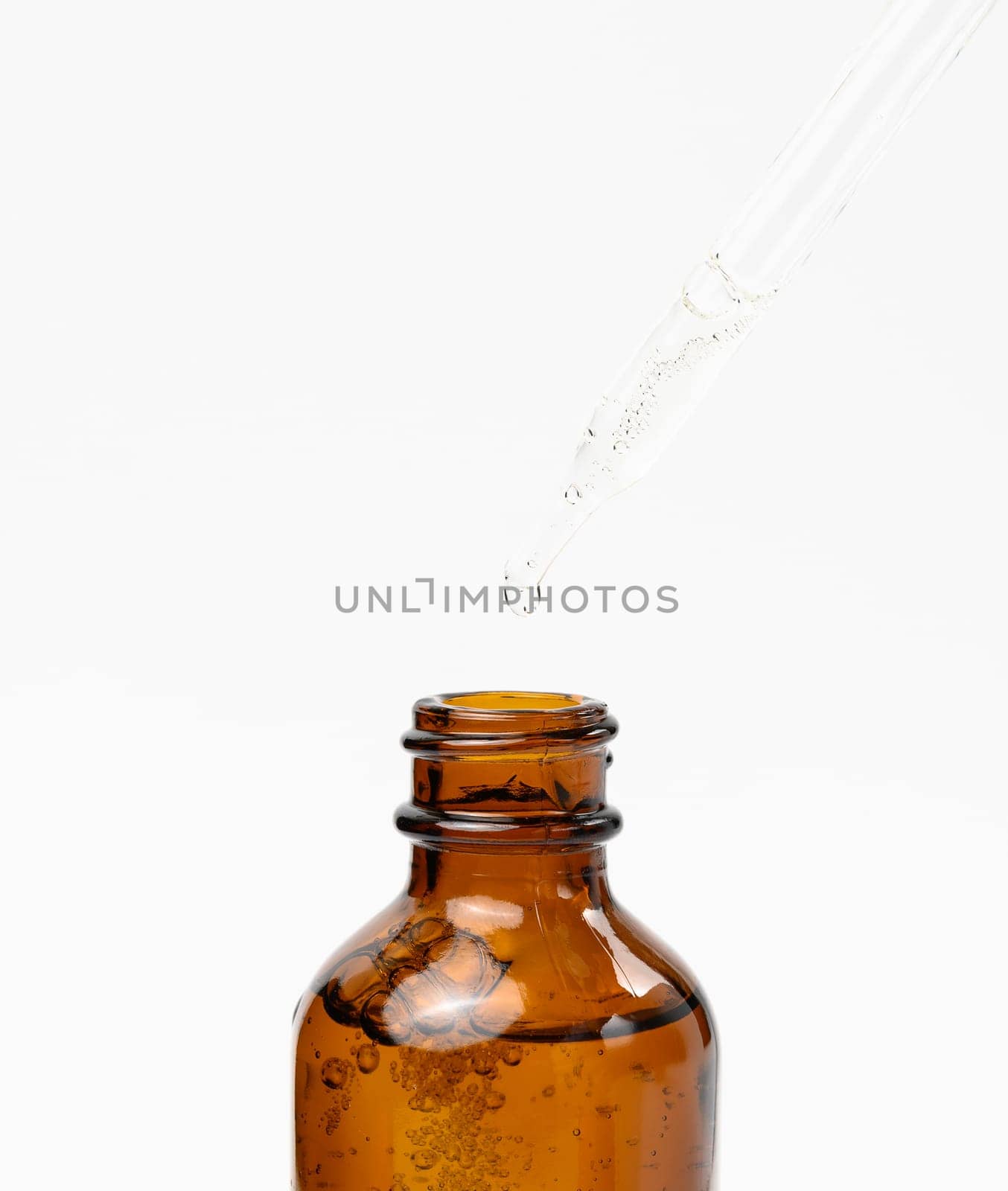 Essential oil falling from the amber glass dropper. Blue bottle of cosmetic oil with a pipette, white background