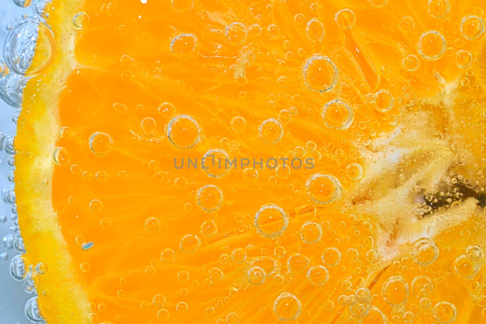 Slice of orange fruit in sparkling water. Orange fruit slice covered by bubbles in carbonated water. Orange fruit slice in water with bubbles. Close-up, macro horizontal image. by roman_nerud