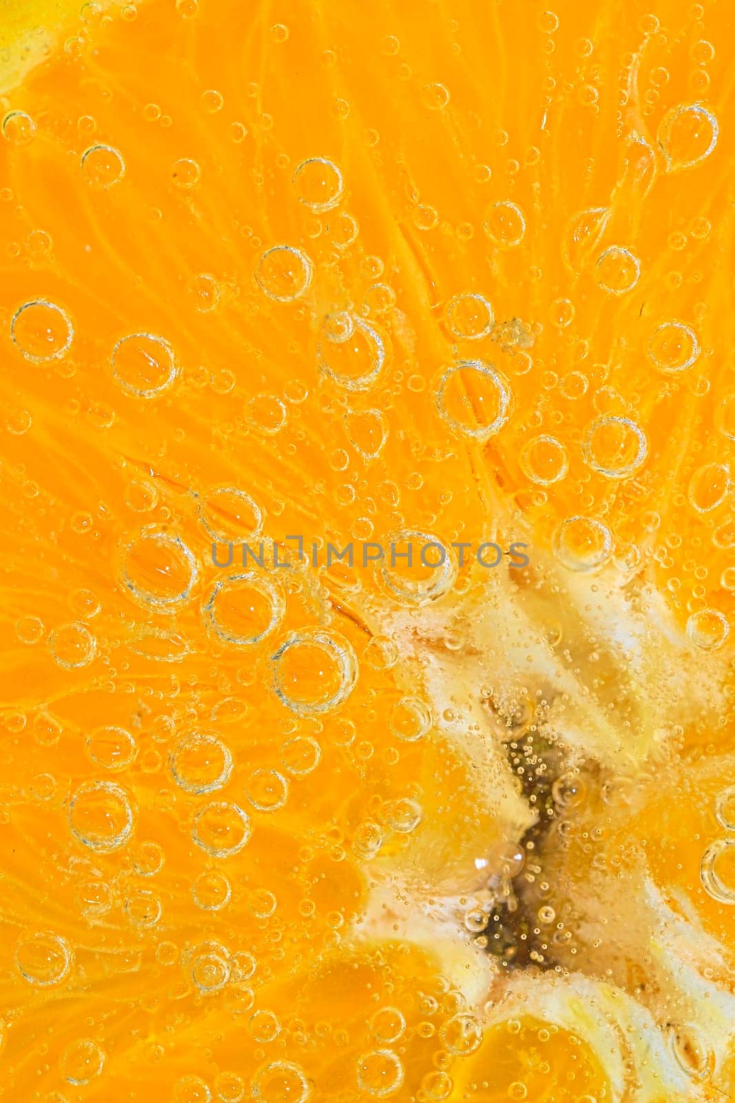 Slice of ripe orange fruit in water. Close-up of orange fruit in liquid with bubbles. Slice of ripe orange fruit in sparkling water. Macro image of fruit in carbonated water