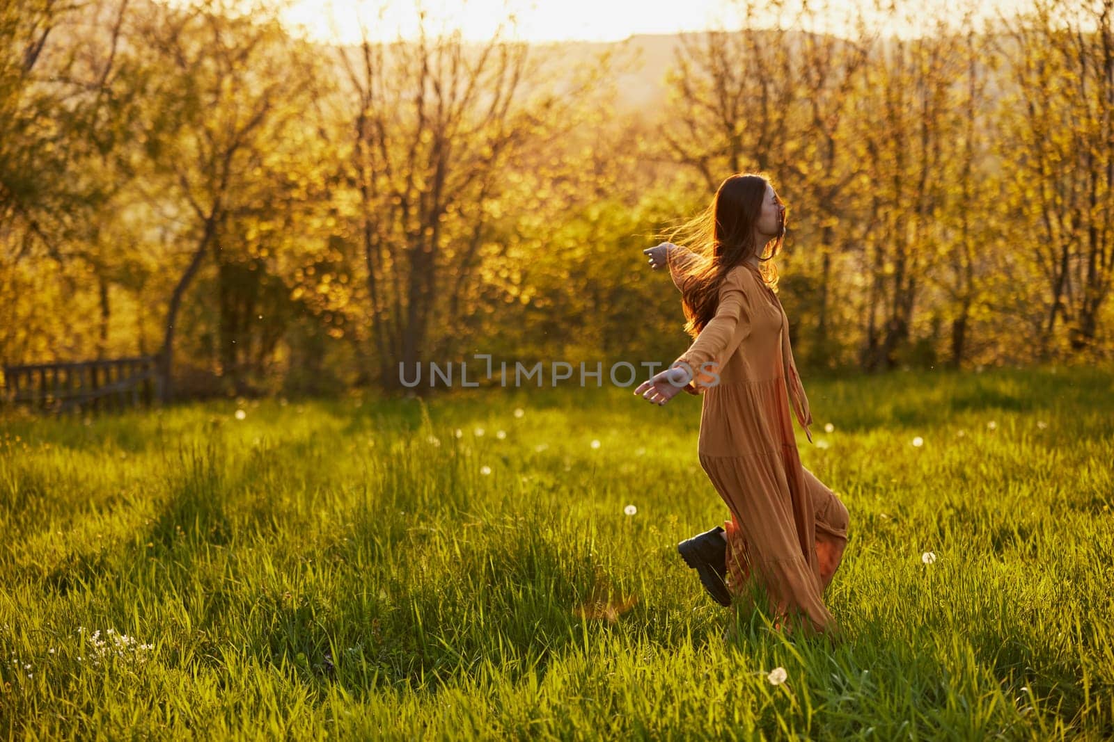 a joyful woman runs through a green field during the sunset enjoying a warm summer day and nature. Horizontal photography in nature by Vichizh