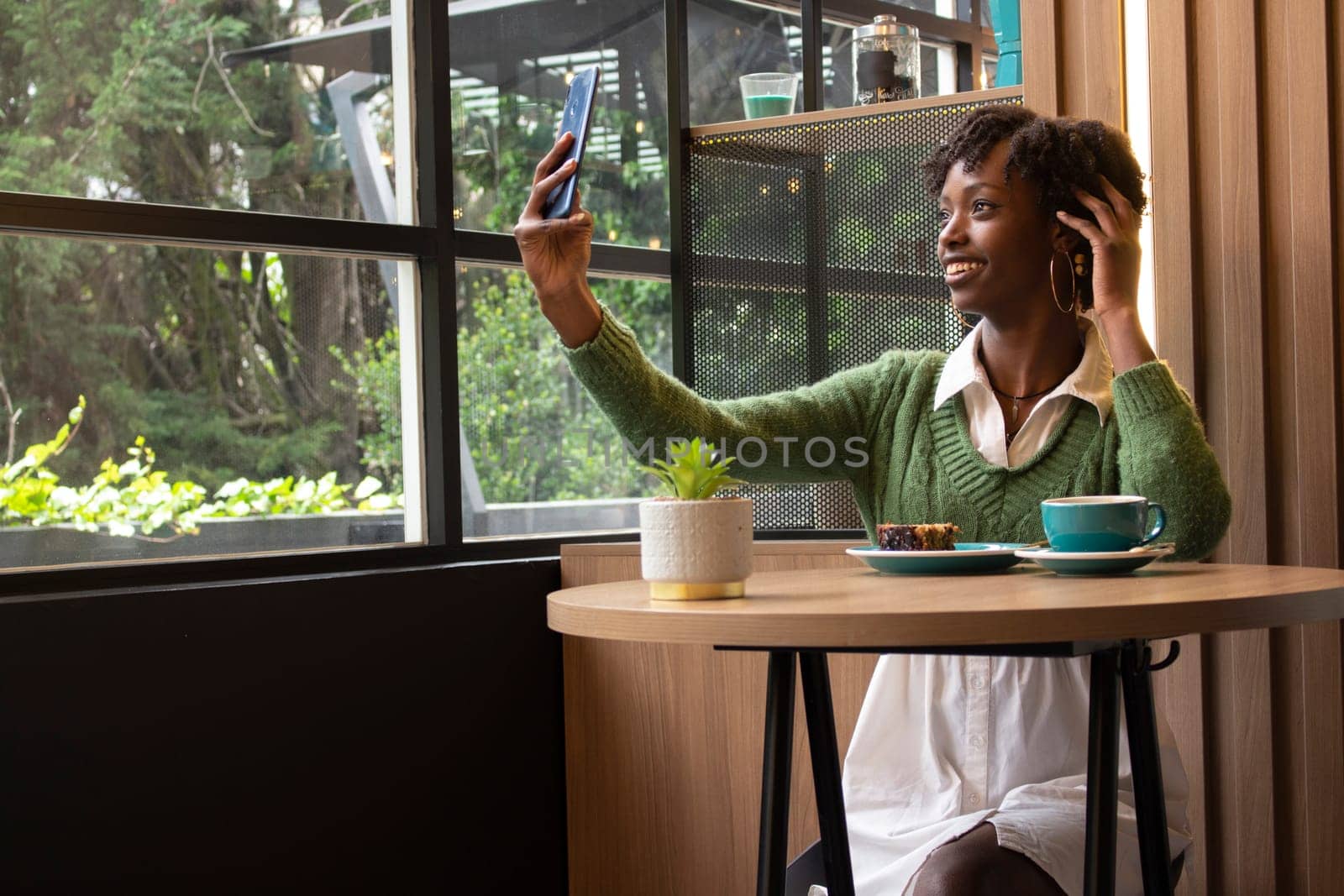 young african american woman sitting in a cafeteria taking a selfie while having a coffee in the city. High quality photo