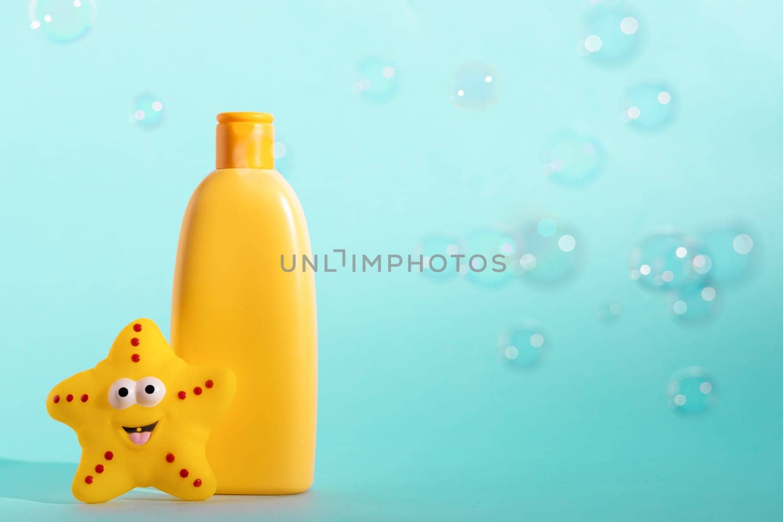 A mock up of a yellow bottle with cosmetic and bath accessories. Kid's shower gel with a place for logo