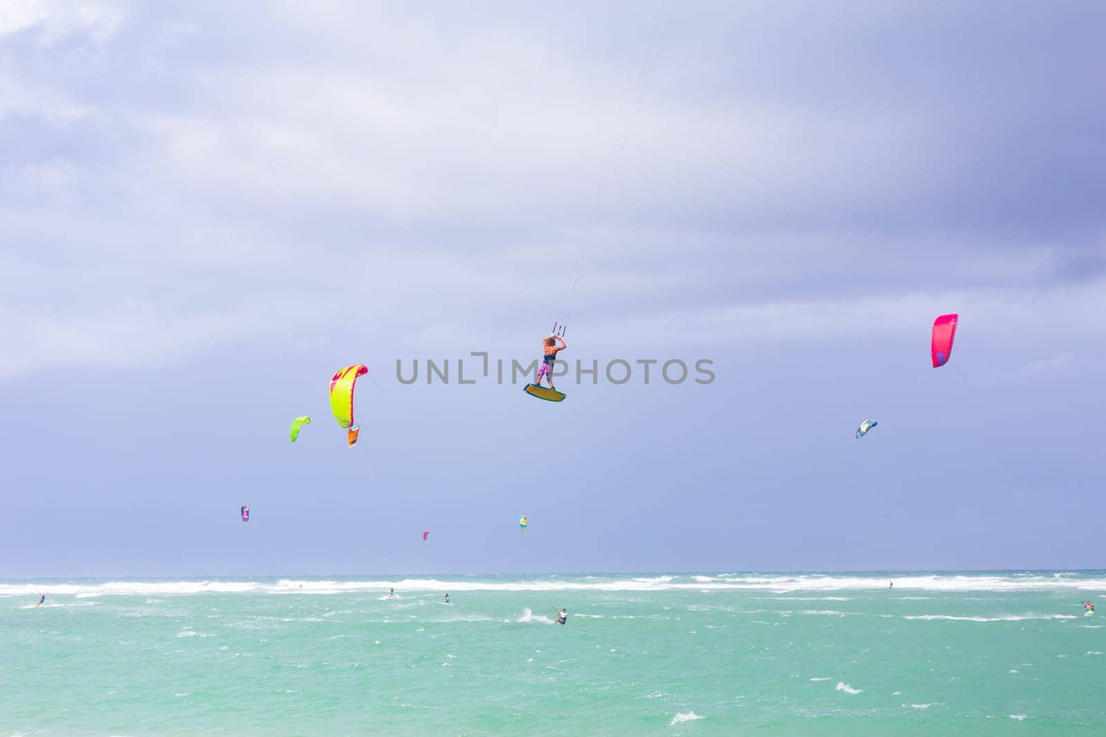 Kiteboarding. Fun in the ocean. Extreme Sport Kitesurfing. Kitesurfer jumping high in the air performing triks during kitesurfing session. by kasto