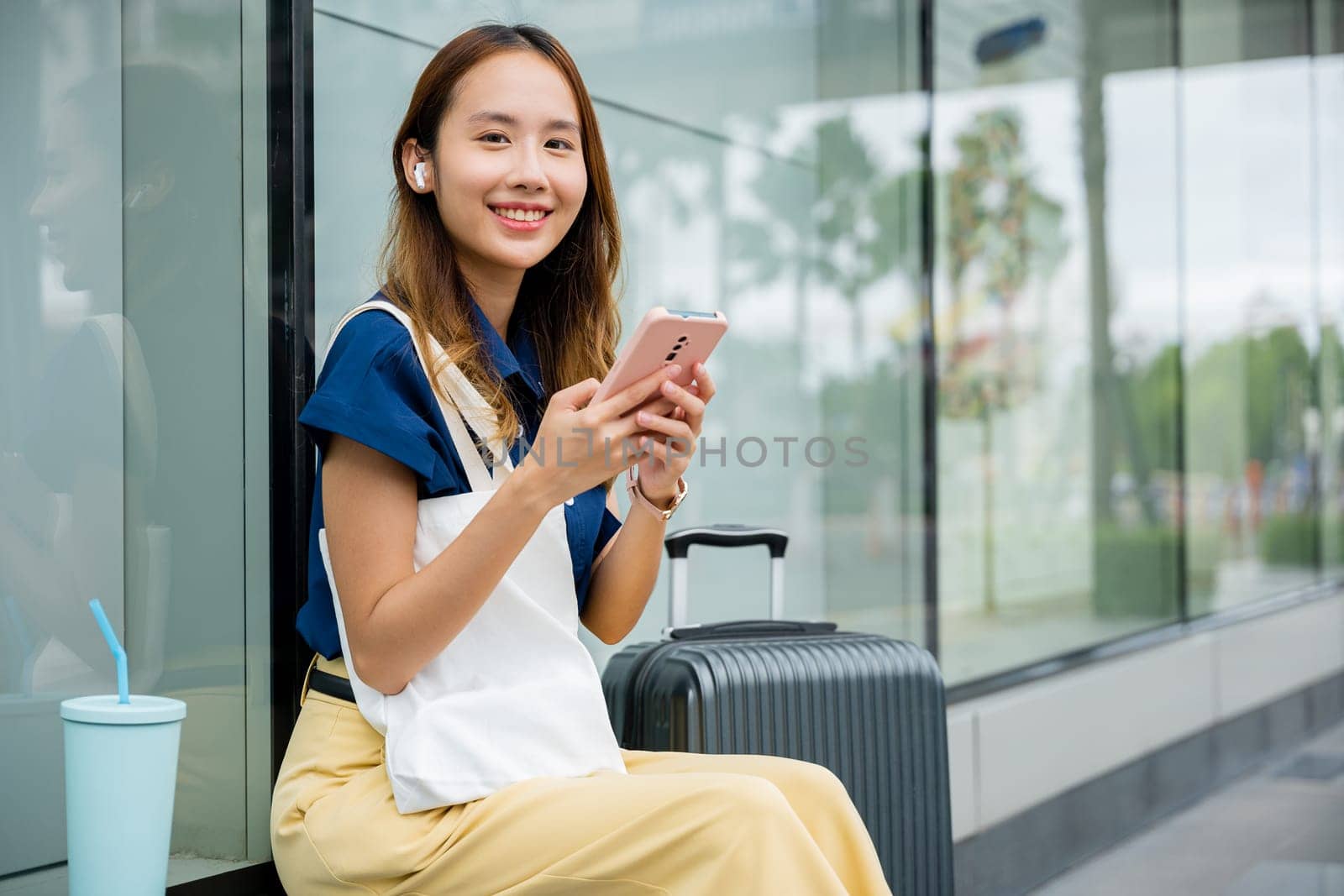 woman sitting with her suitcase, using her mobile phone to send messages and stay connected by Sorapop