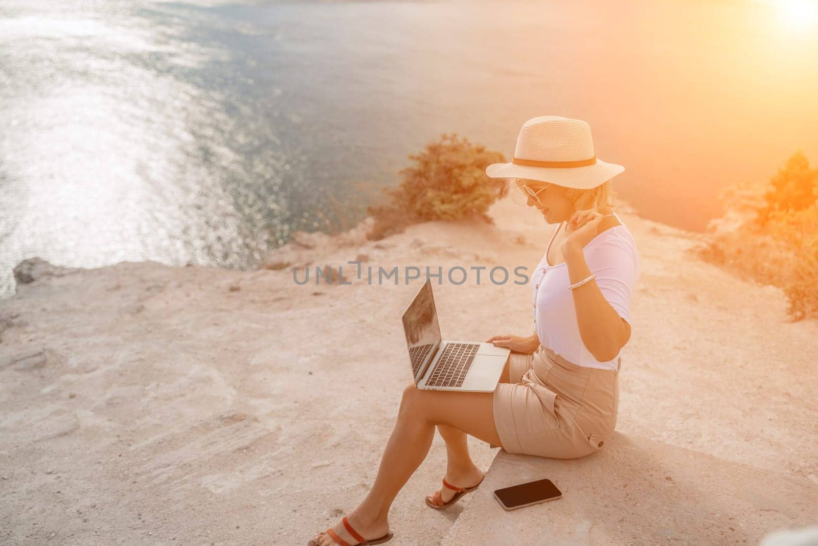 Freelance women sea working on the computer. Good looking middle aged woman typing on a laptop keyboard outdoors with a beautiful sea view. The concept of remote work. by Matiunina