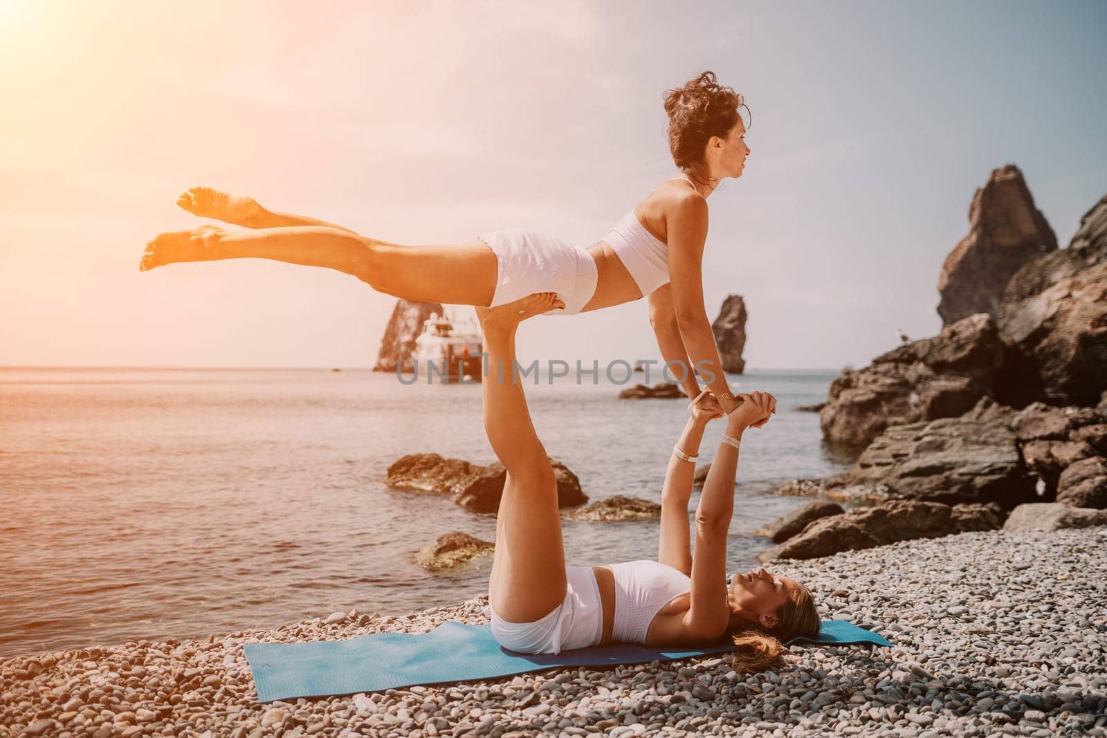 Woman sea yoga. Two happy women practicing yoga on the beach with ocean and rock mountains. Motivation and inspirational fit and exercising. Healthy lifestyle outdoors in nature, fitness concept. by panophotograph
