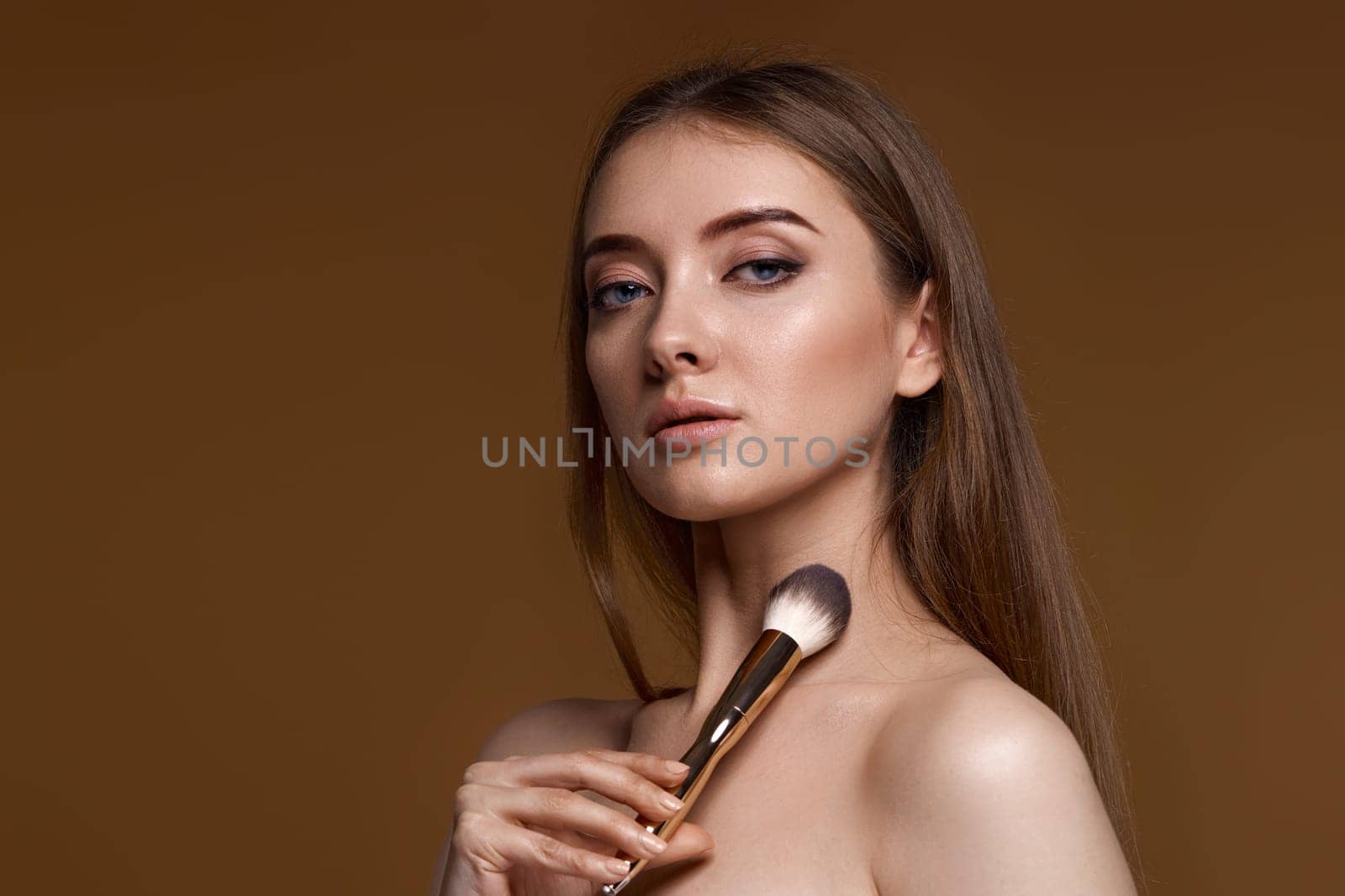 young woman applying blush on cheeks with make-up brush on beige background. copy space