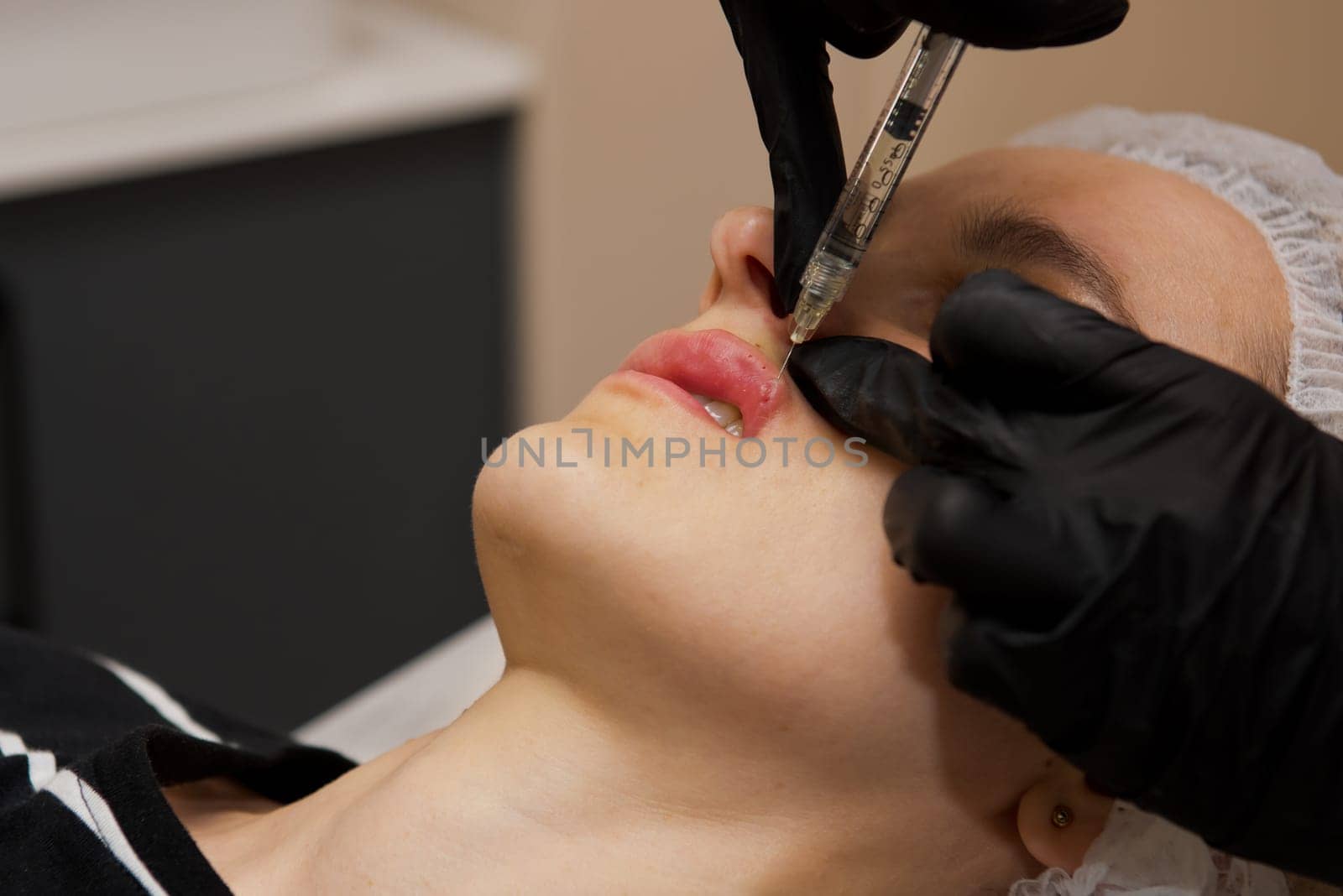Beauty injections. Young woman receiving a injection in her lips. Selective focus.