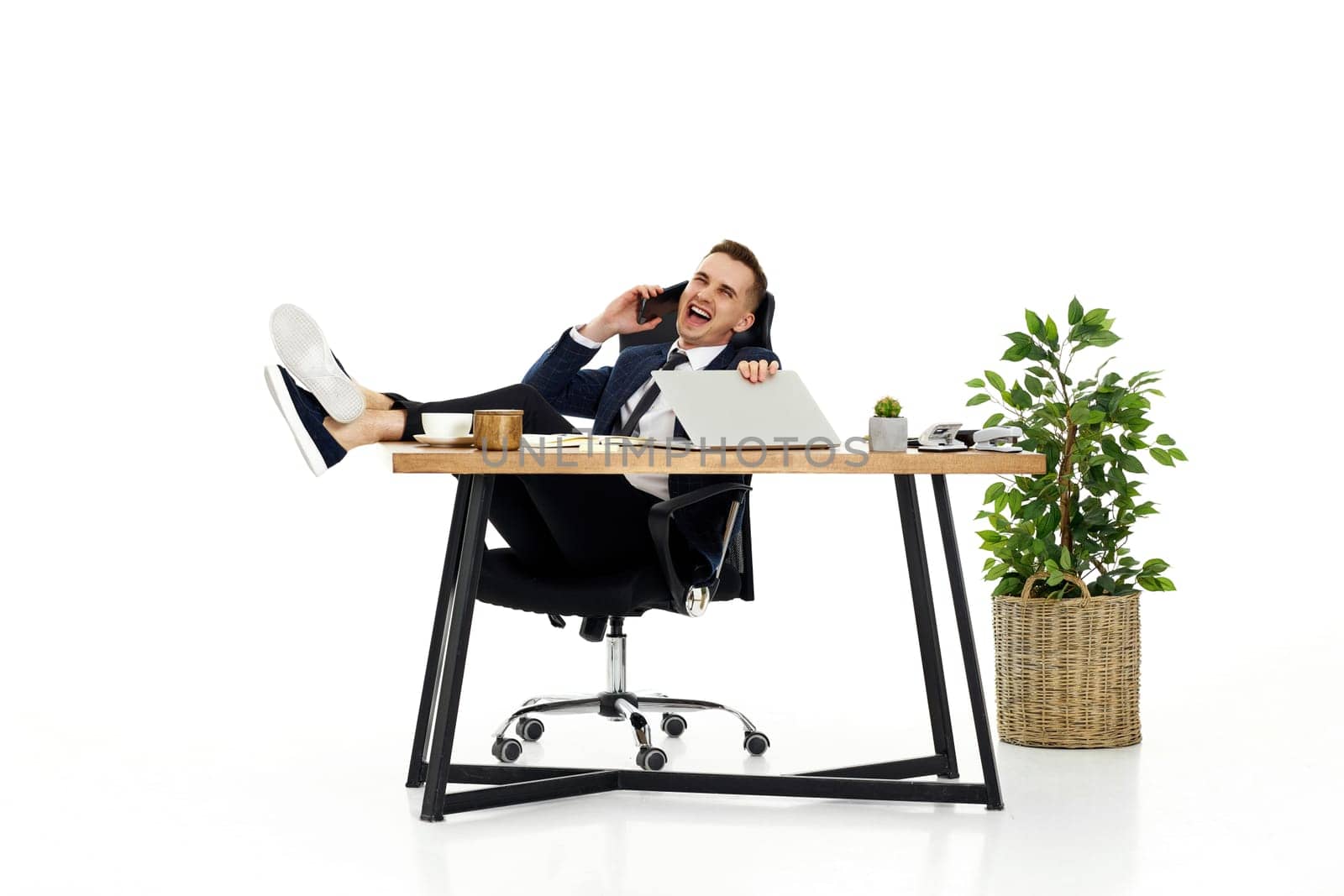Successful happy businessman working with laptop and having phone conversation with client