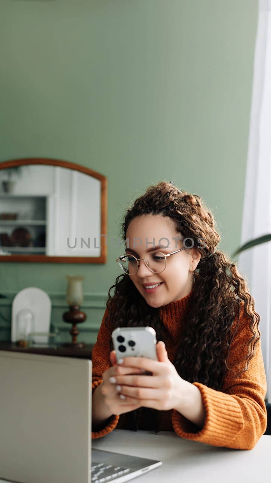 Smiling Young woman using smartphone for remote work and e-learning at home. Modern Technology: Young Woman Using Smartphone for Work and Learning at Home. Pretty woman holding mobile phone.