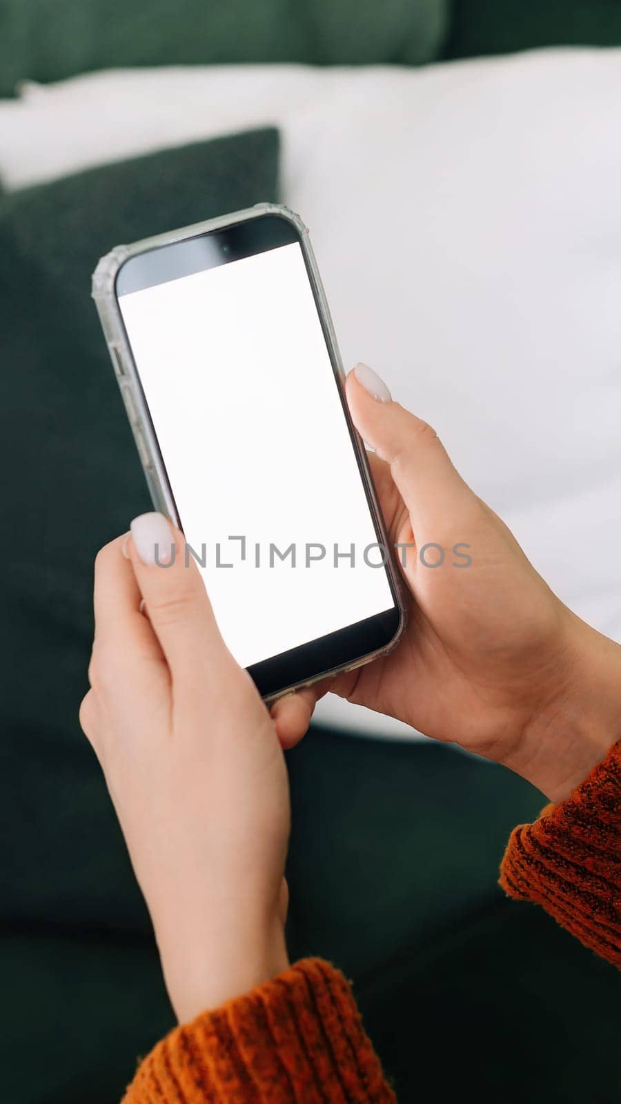 Over shoulder view of woman holding smartphone with white mock up cellular screen in hands using mobile apps on cell phone relaxing on sofa at home. Cellphone display mock up for advertising concept