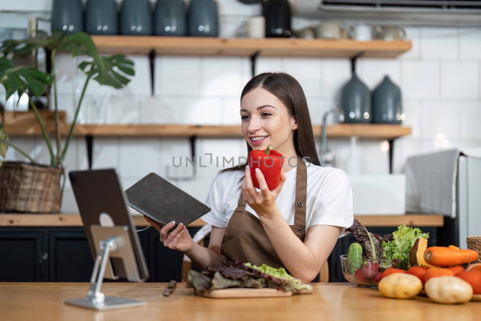 Image of young pretty lady in kitchen and cooking the salad. Looking at tablet computer.