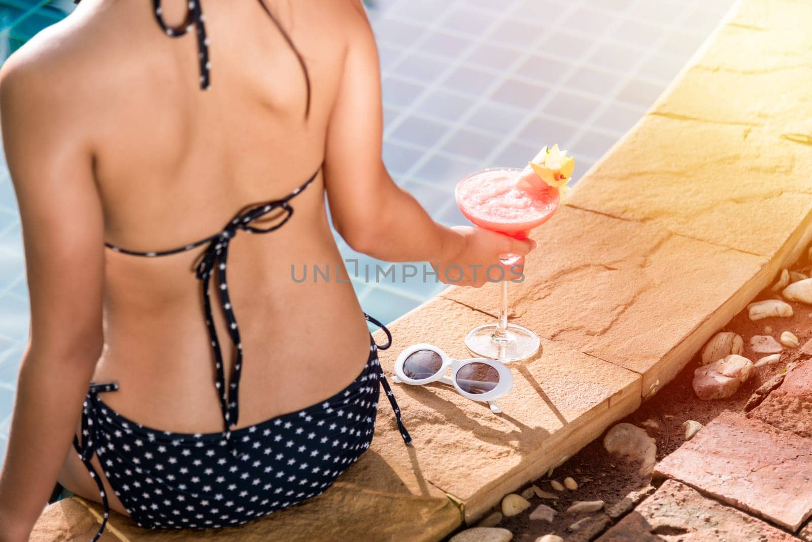 Portrait elegant young woman relaxed in bikini drinking beverage on vacation at poolside blue water, Brunette girl enjoying with cocktails in swimming pool, vacation on summer season. Back view