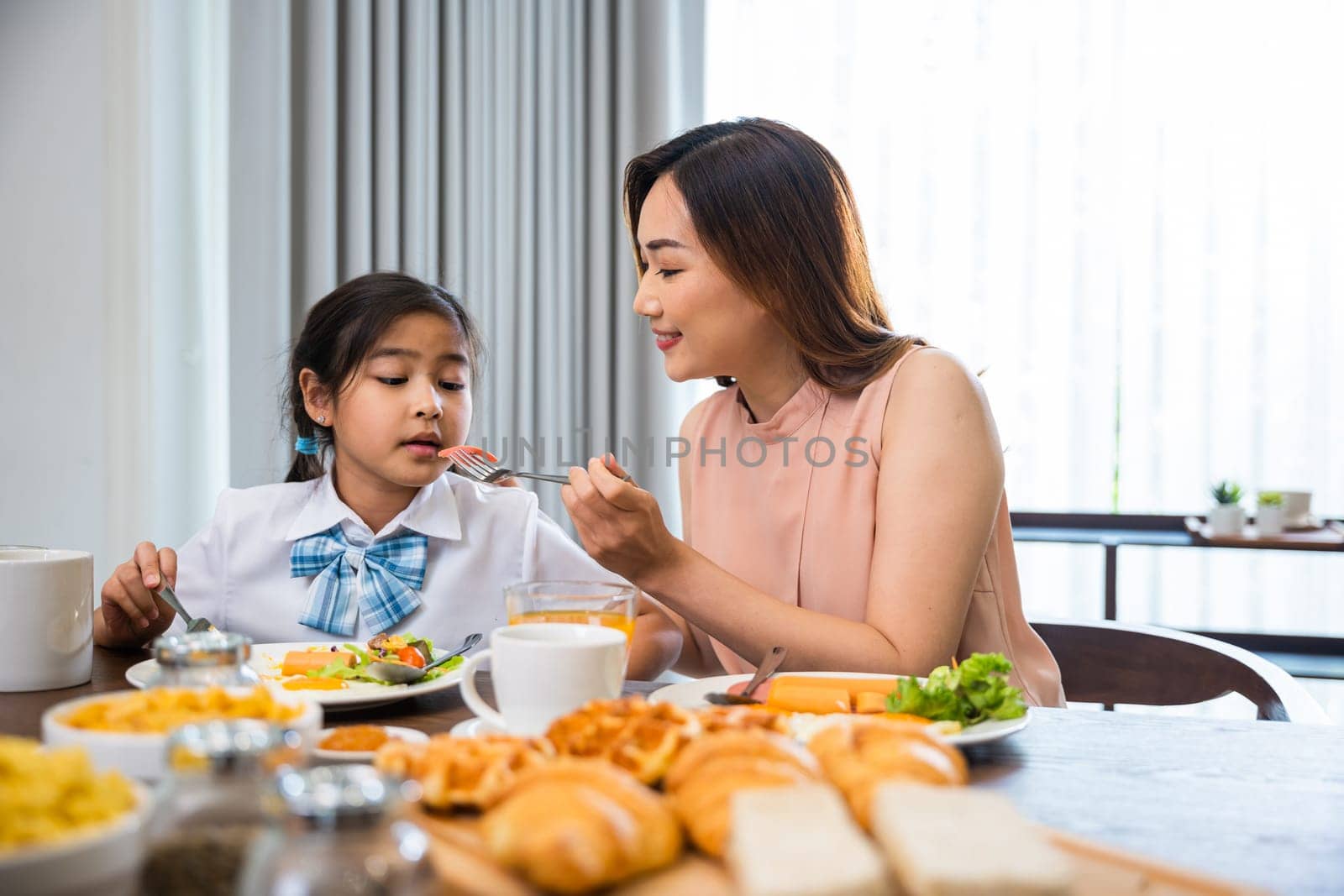 Asian family breakfast. smiling mother and child daughter having breakfast on food table, Healthy food at home before go to school, Mom and little preschooler have fun eating meal together