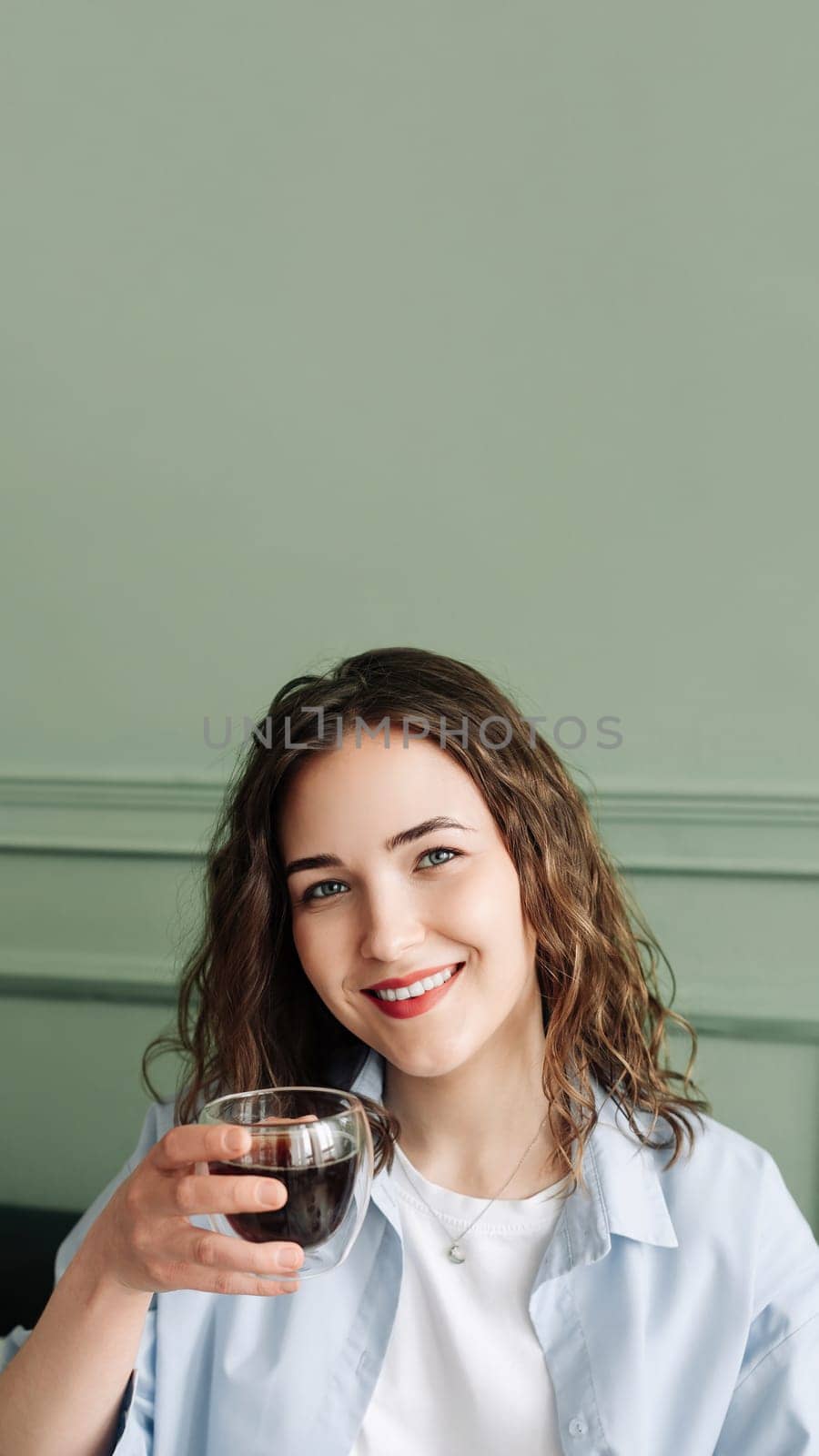 Happy young woman housewife enjoying a cozy break with hot tea on the sofa at home. Smiling lady relaxing with a warm drink and looking at the camera in a close-up indoor portrait