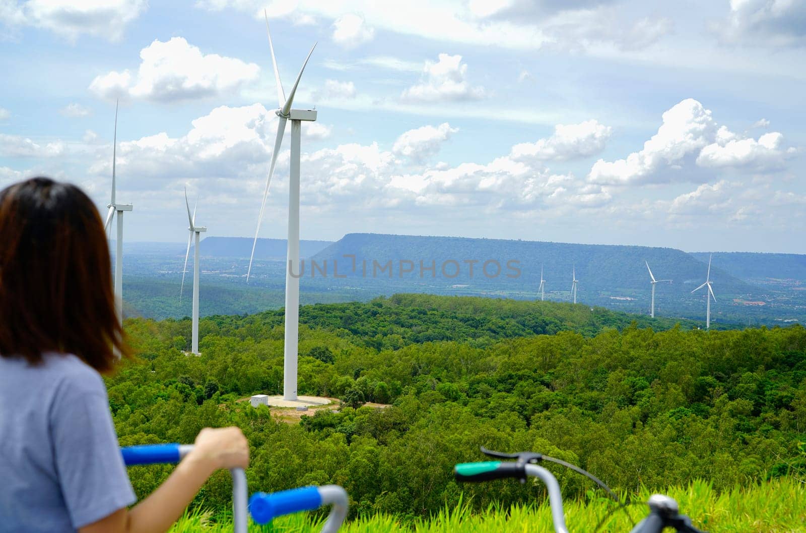 Wind farm with woman riding bike in foreground. Wind energy. Wind power. Sustainable, renewable energy. Wind turbines generate electricity. Green technology. Sustainable resources. Energy security.                          