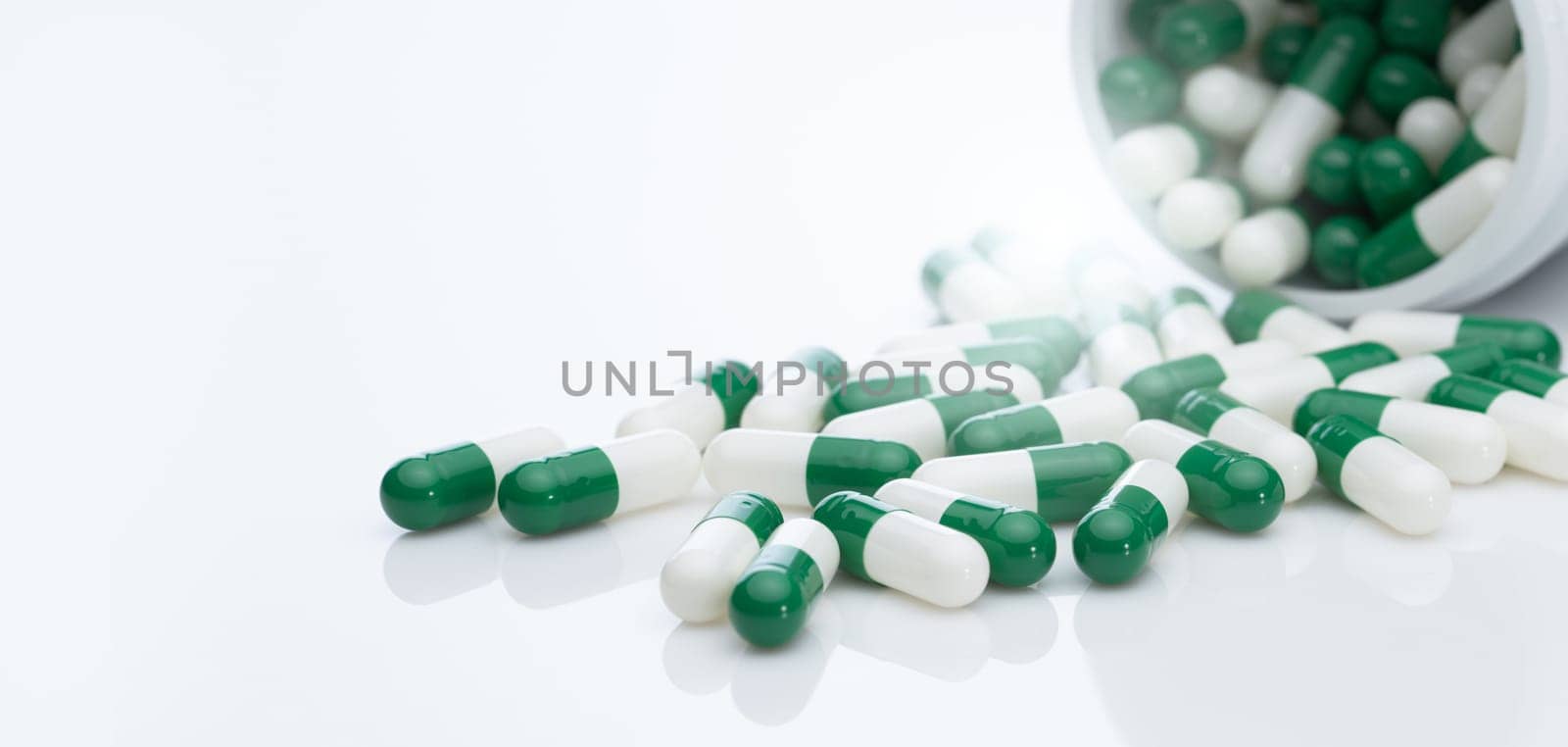 Green and white capsule pill spread out of pill bottle. Healthcare and medicine. Prescription drug. Pharmaceutical industry. Cancer targeted therapy and immunotherapy drug research and development. by Fahroni