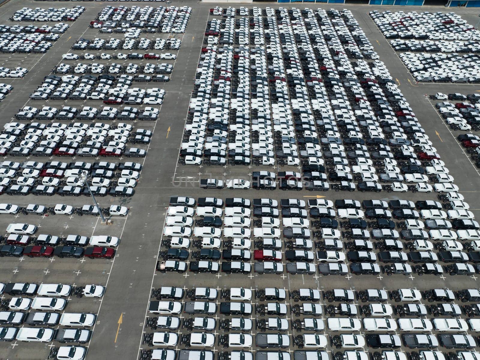 Aerial view of new cars stock at factory parking lot. Above view cars parked in a row. Automotive industry. Logistics business. Import or export new cars at warehouse. Big parking lot at port terminal by Fahroni