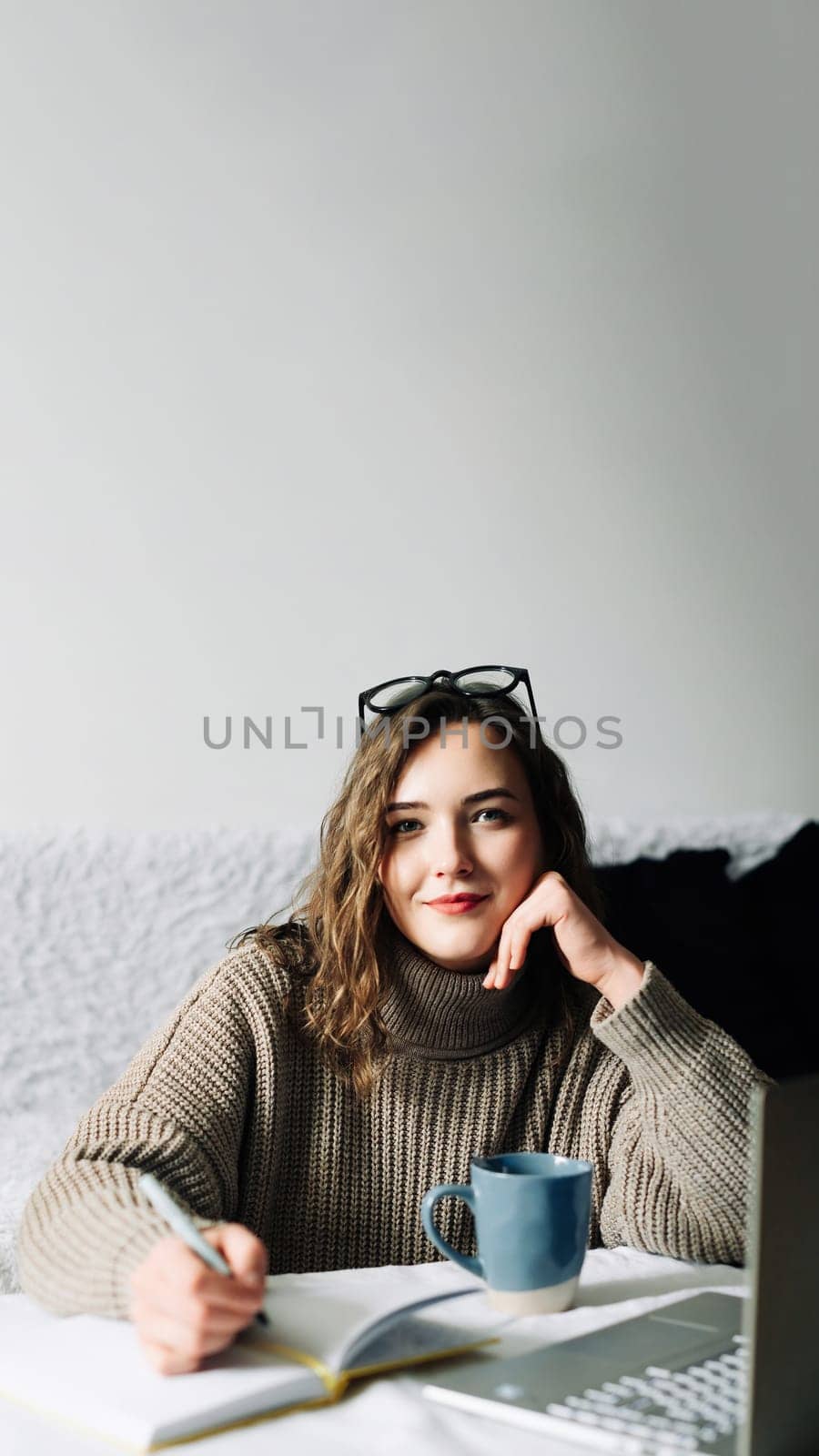 Stylish and focused female PR manager creating content plan for online store, working from home with laptop, notebook and coffee, looking at camera.