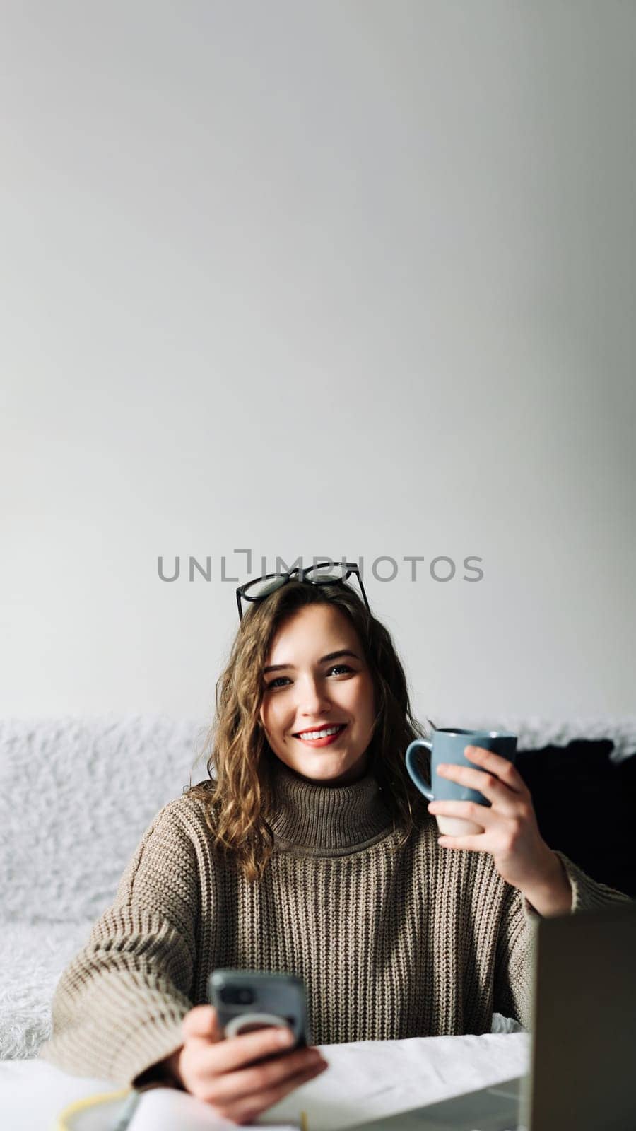 Young student taking a break from online studies, enjoying coffee and phone, laughing at memes and relaxing at kitchen table.