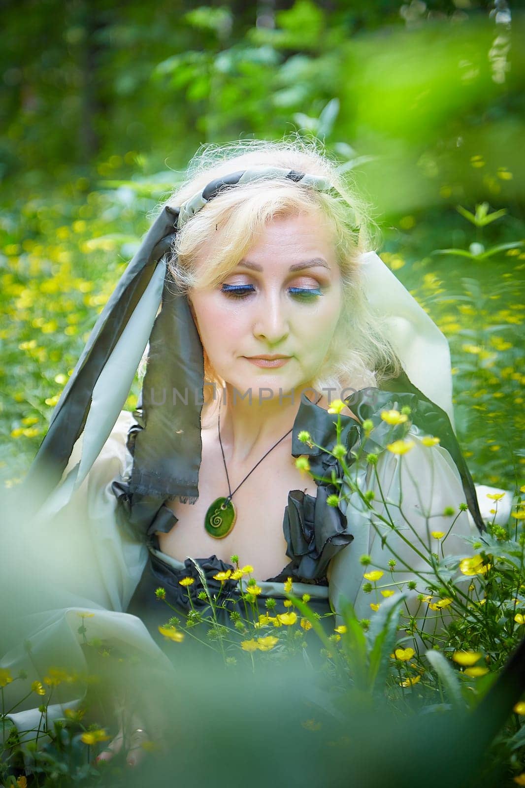 Adult mature woman 40-60 in a green long fairy dress in forest. Photo shoot in style of dryad and queen of nature. Fairy in beautiful green summer forest. Concept of caring for nature