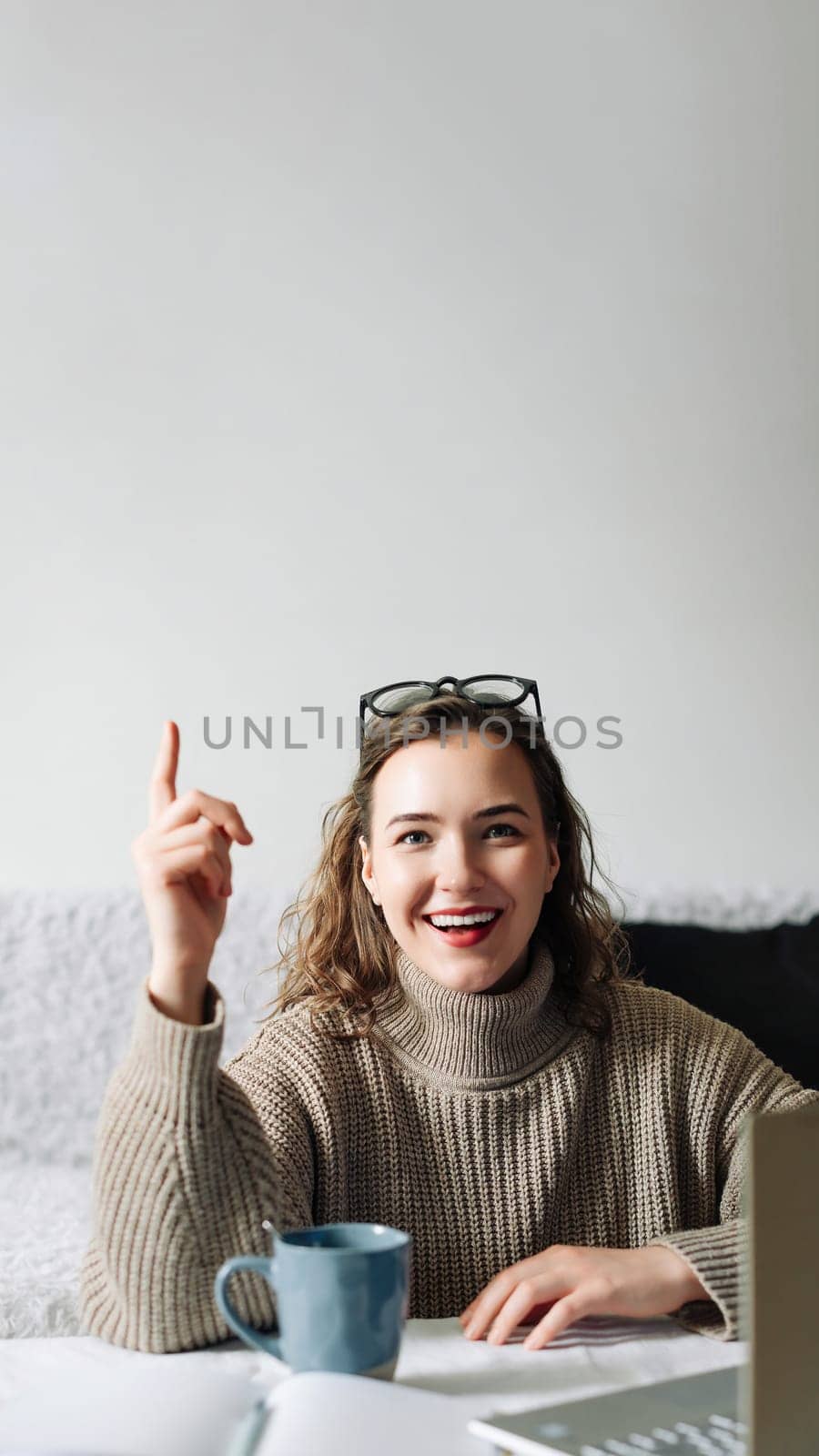 Eureka Excited female entrepreneur with successful business idea, sitting at kitchen table with laptop and showing index finger, ready to make a brilliant project and business plan.
