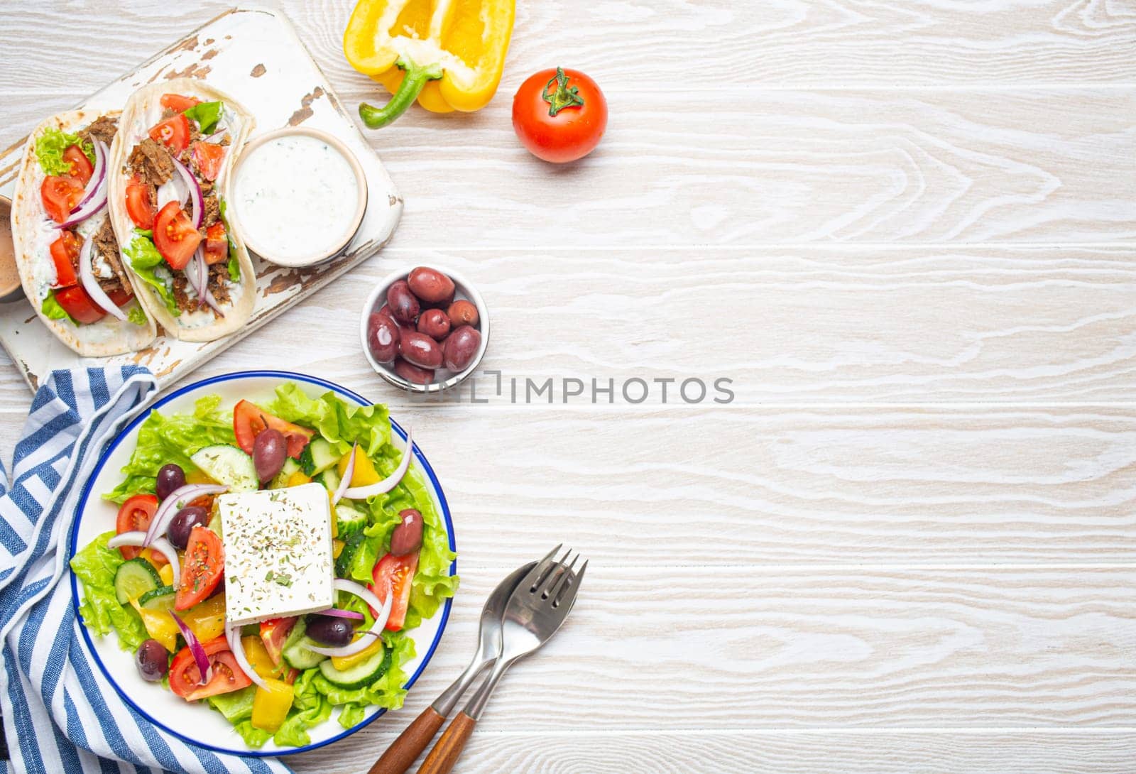 Traditional Greek Food: Greek Salad, Gyros with meat and vegetables, Tzatziki sauce, Olives on White rustic wooden table background from above. Cuisine of Greece. Copy space