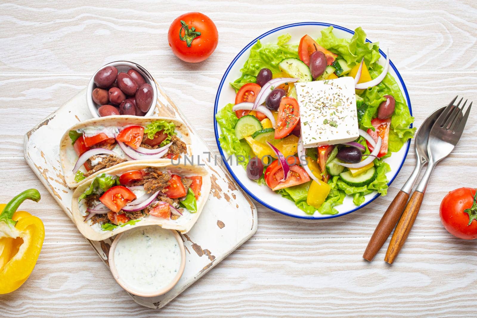 Traditional Greek Food: Greek Salad, Gyros with meat and vegetables, Tzatziki sauce, Olives on White rustic wooden table background top view. Cuisine of Greece
