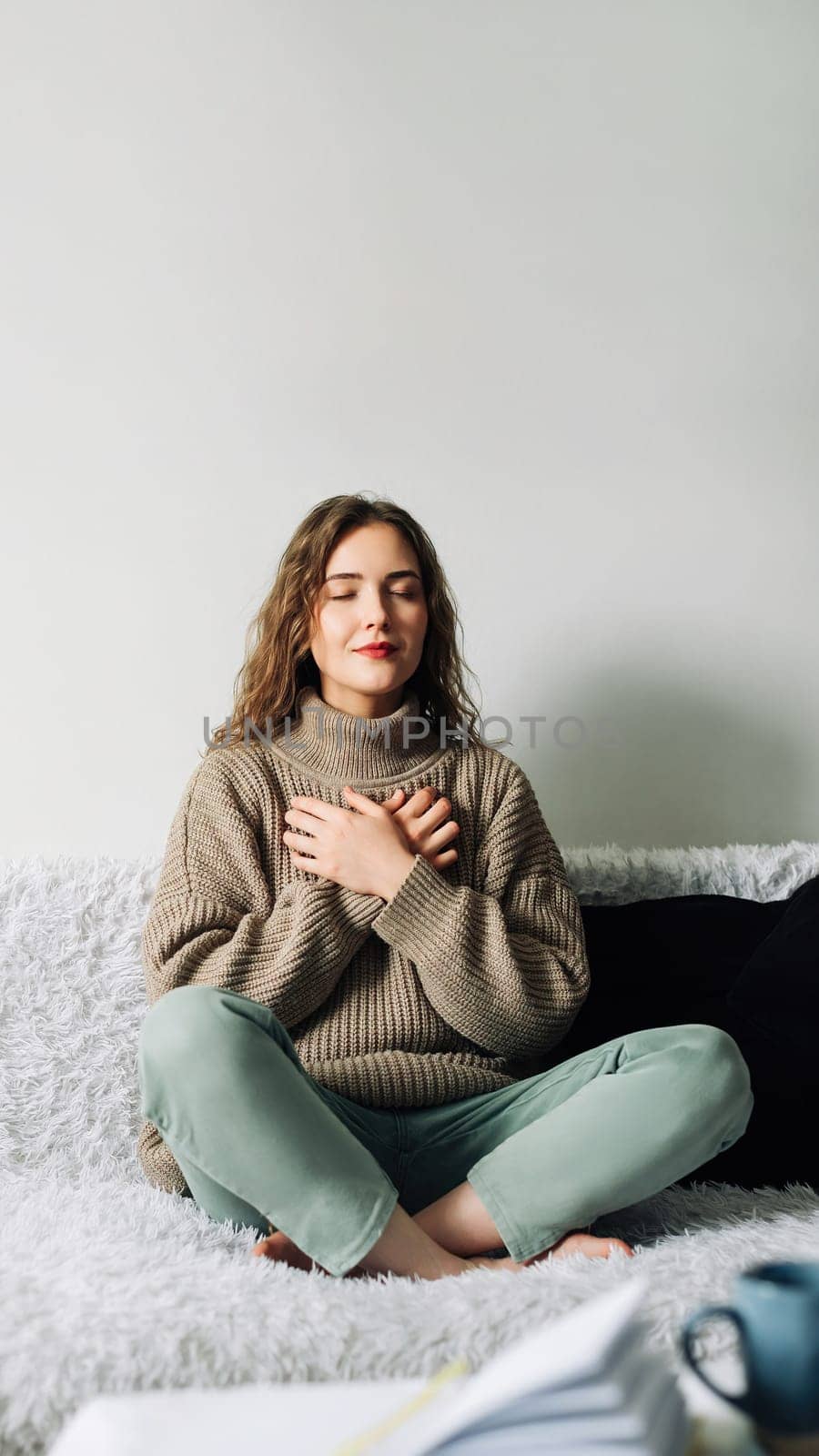 Beautiful young woman in lotus pose on bed practicing pranayama breathing techniques, finding inner balance after a stressful day.