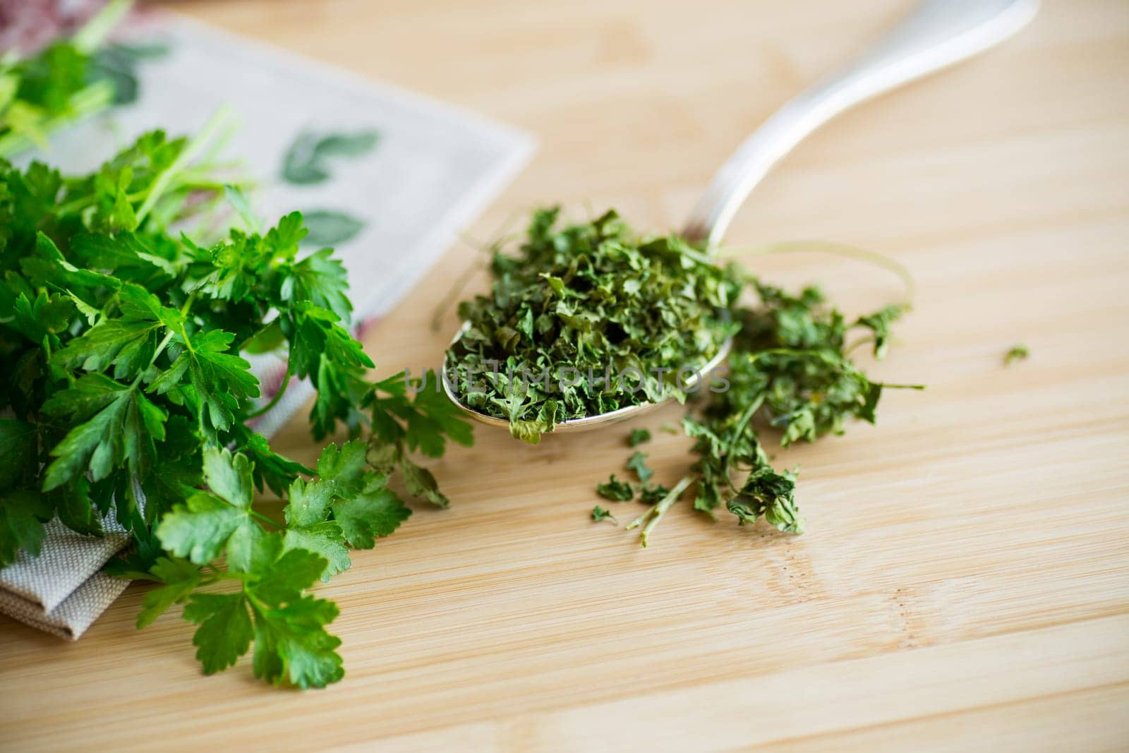 dried parsley in a spoon on a wooden table next to fresh herbs.