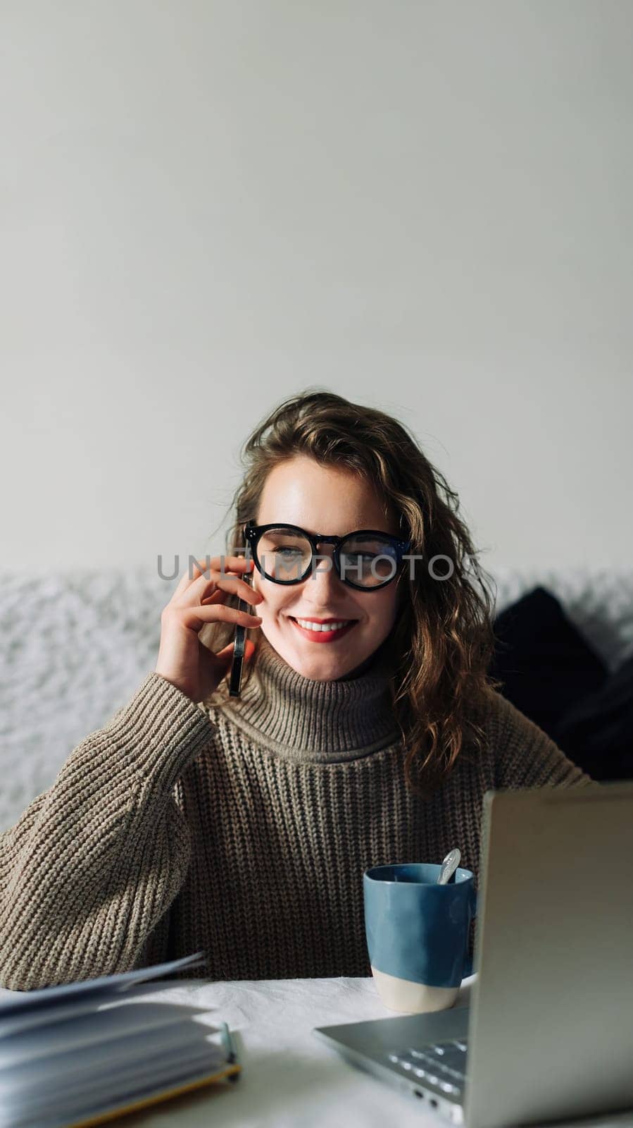 Young accountant manager working at home at the kitchen table, talking on the phone in front of the laptop, smiling, cute talking to CEO or bank support team about corporate account.