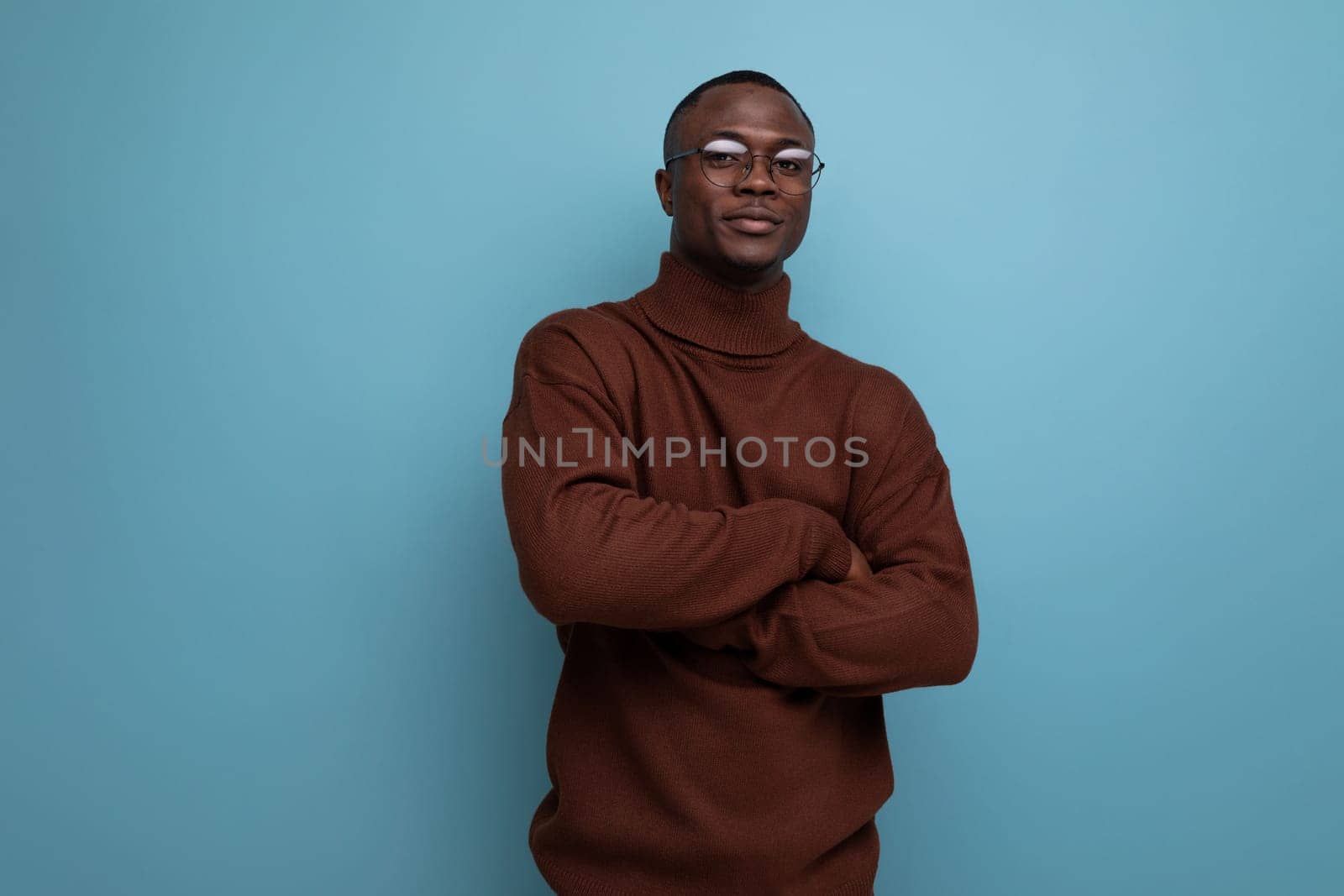 elegant young american brunet man in stylish brown sweater posing over isolated blue background with copy space by TRMK