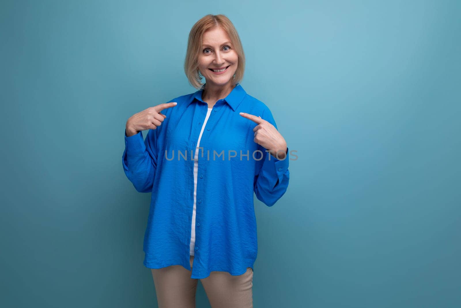 joyful smiling 50s middle aged woman in a blue shirt on a blue background with copy space.