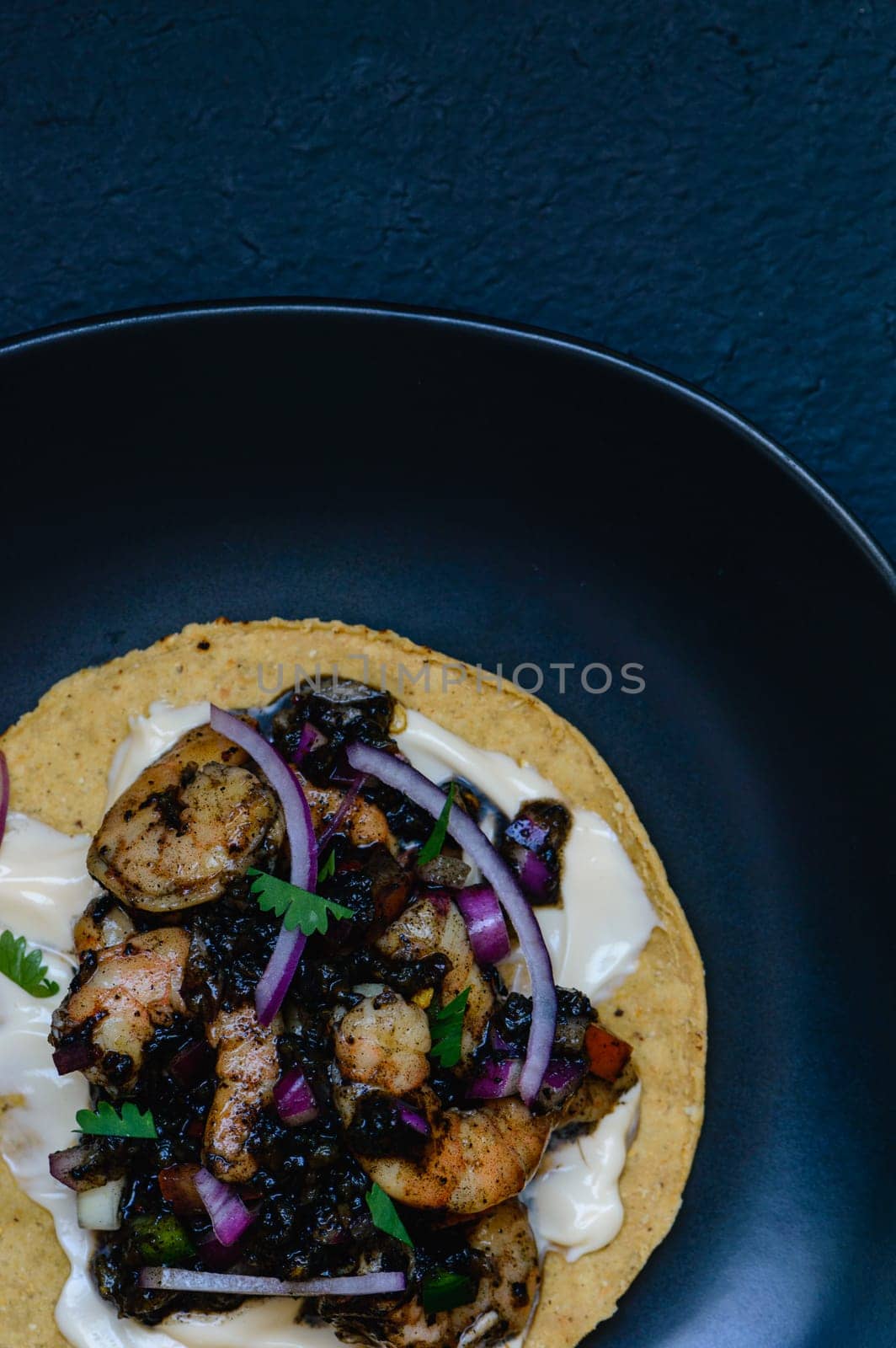 Black shrimp ceviche, Mexican seafood dish made with fresh shrimp, chili ashes and lime juice. Served on a crispy corn tostada and shot on black background.