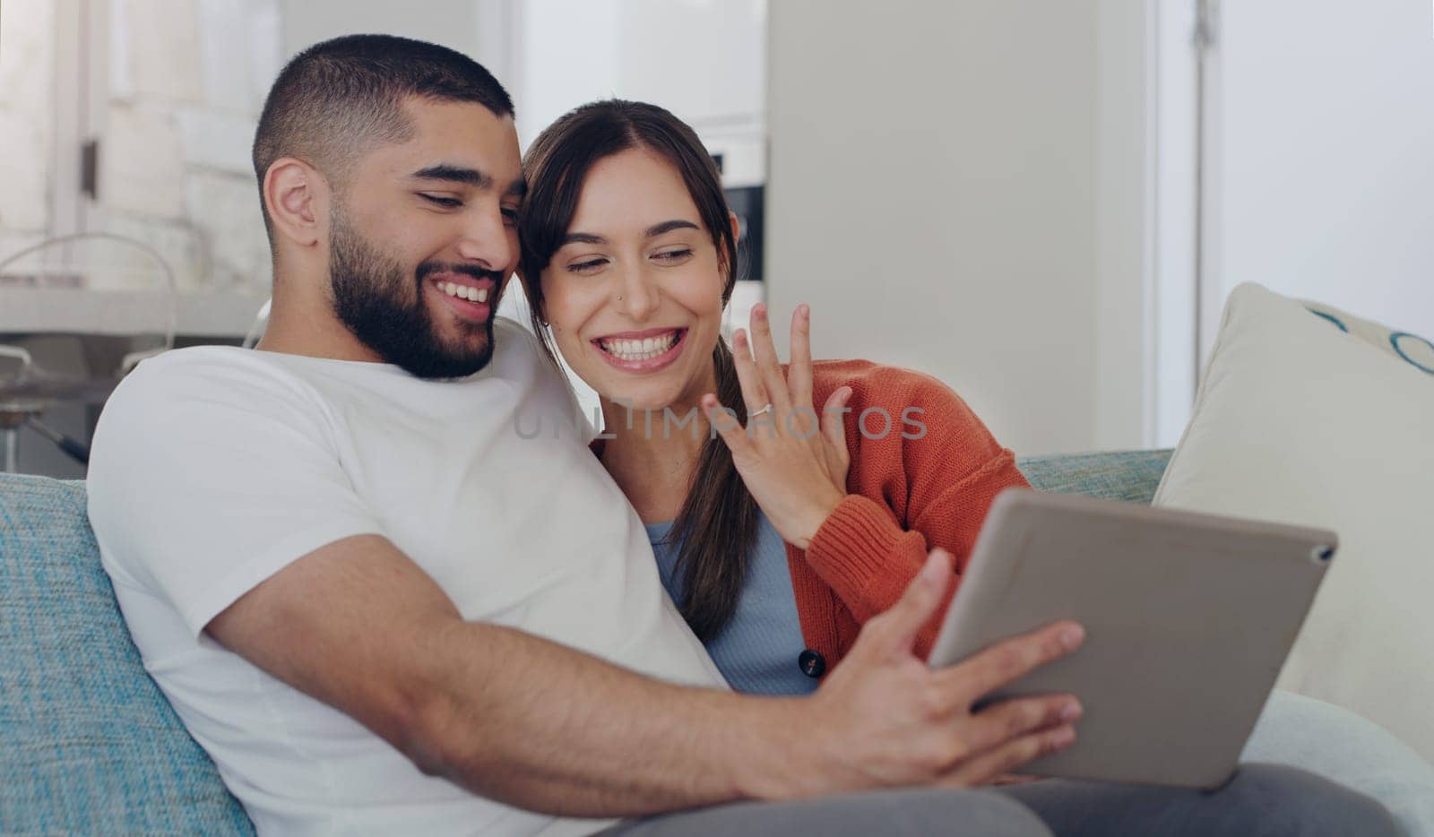 Engagement, announcement and a couple on a video call from a sofa in the living room of their home together. Smile, proud or excited with a happy man and woman sharing good news about their marriage by YuriArcurs