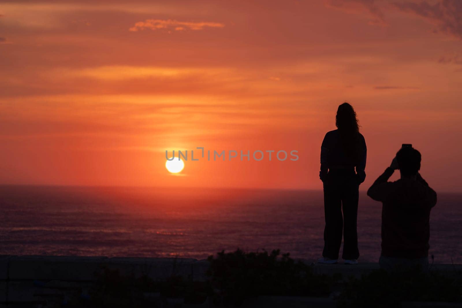 romantic lovers couple silhouettes. Beach photo shooting at sunset, man taking pictures of woman.