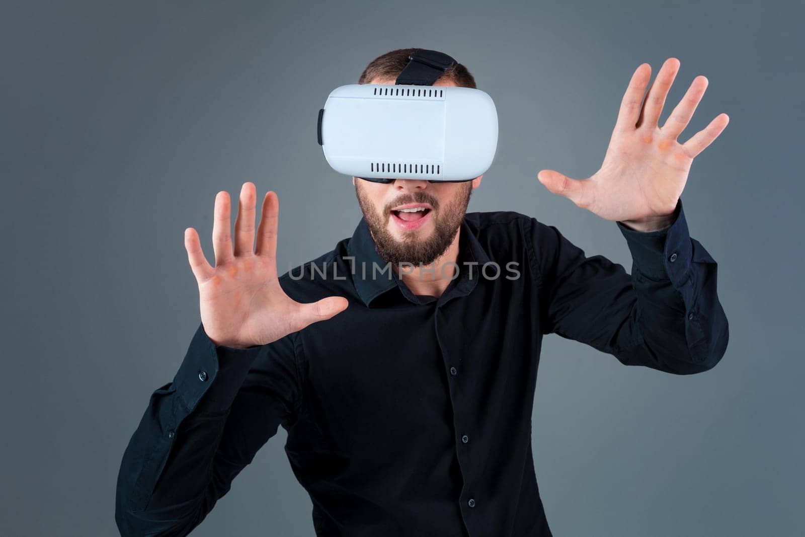 Emotional young man using a VR headset and experiencing virtual reality on grey background. A man dressed in a black shirt