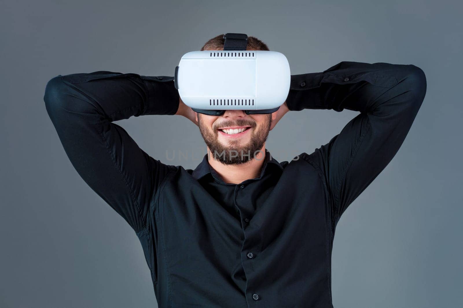 Emotional young man using a VR headset and experiencing virtual reality on grey background. A man dressed in a black shirt