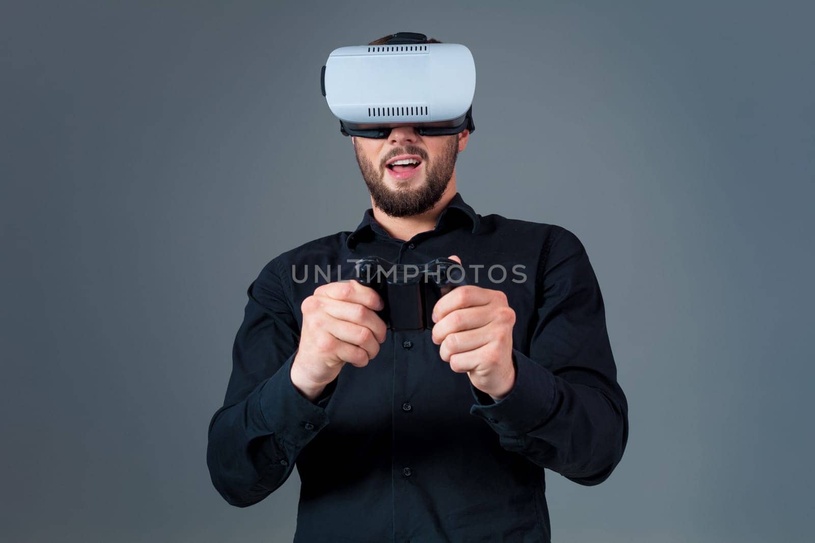 Emotional young man using a VR headset and experiencing virtual reality on grey background. A man dressed in a black shirt