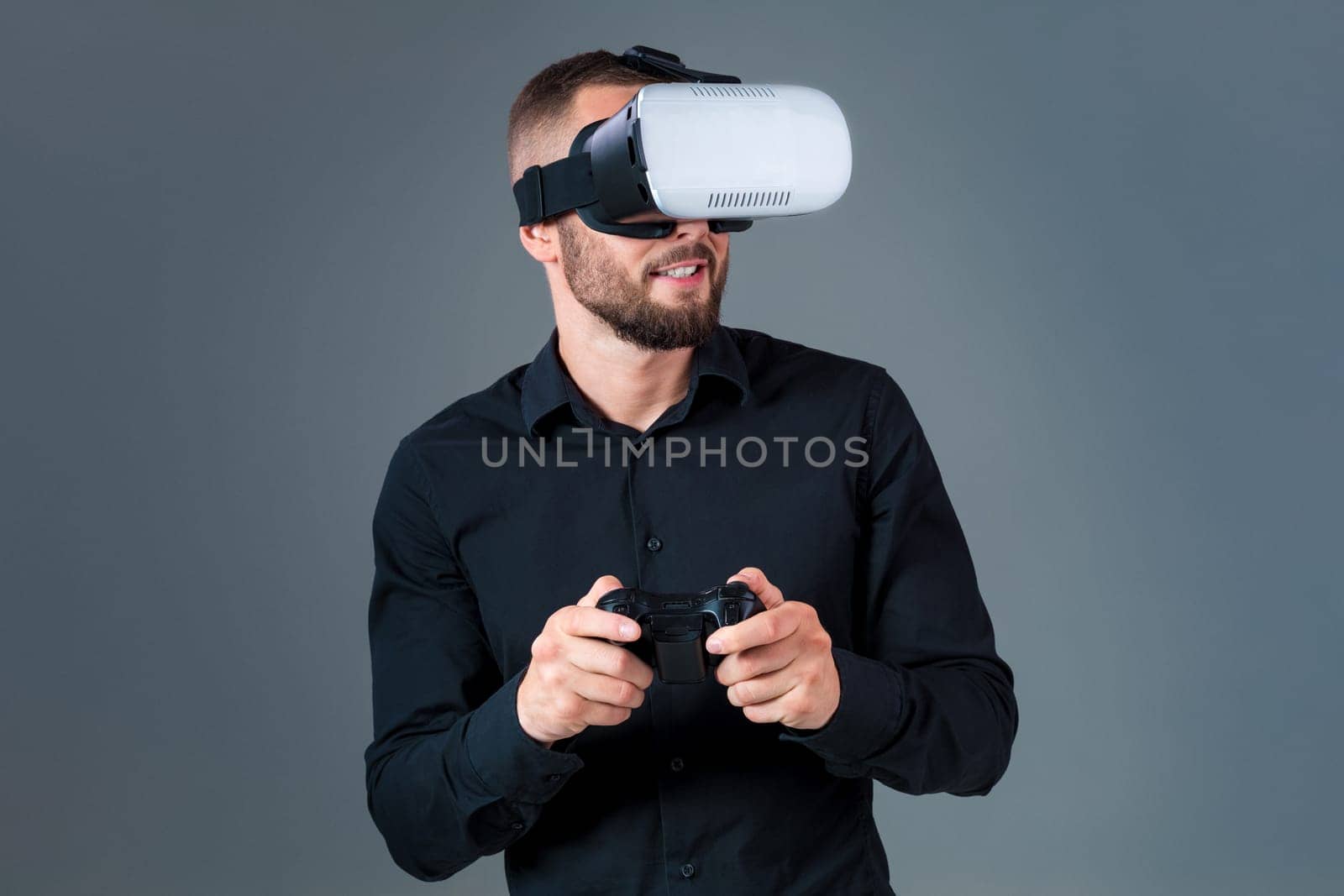 Emotional young man using a VR headset and experiencing virtual reality on grey background. A man dressed in a black shirt