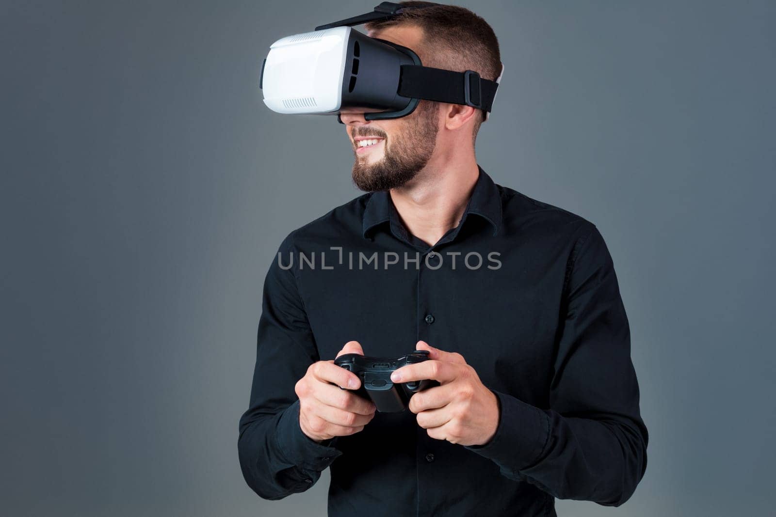 Emotional young man using a VR headset and experiencing virtual reality on grey background. A man dressed in a black shirt