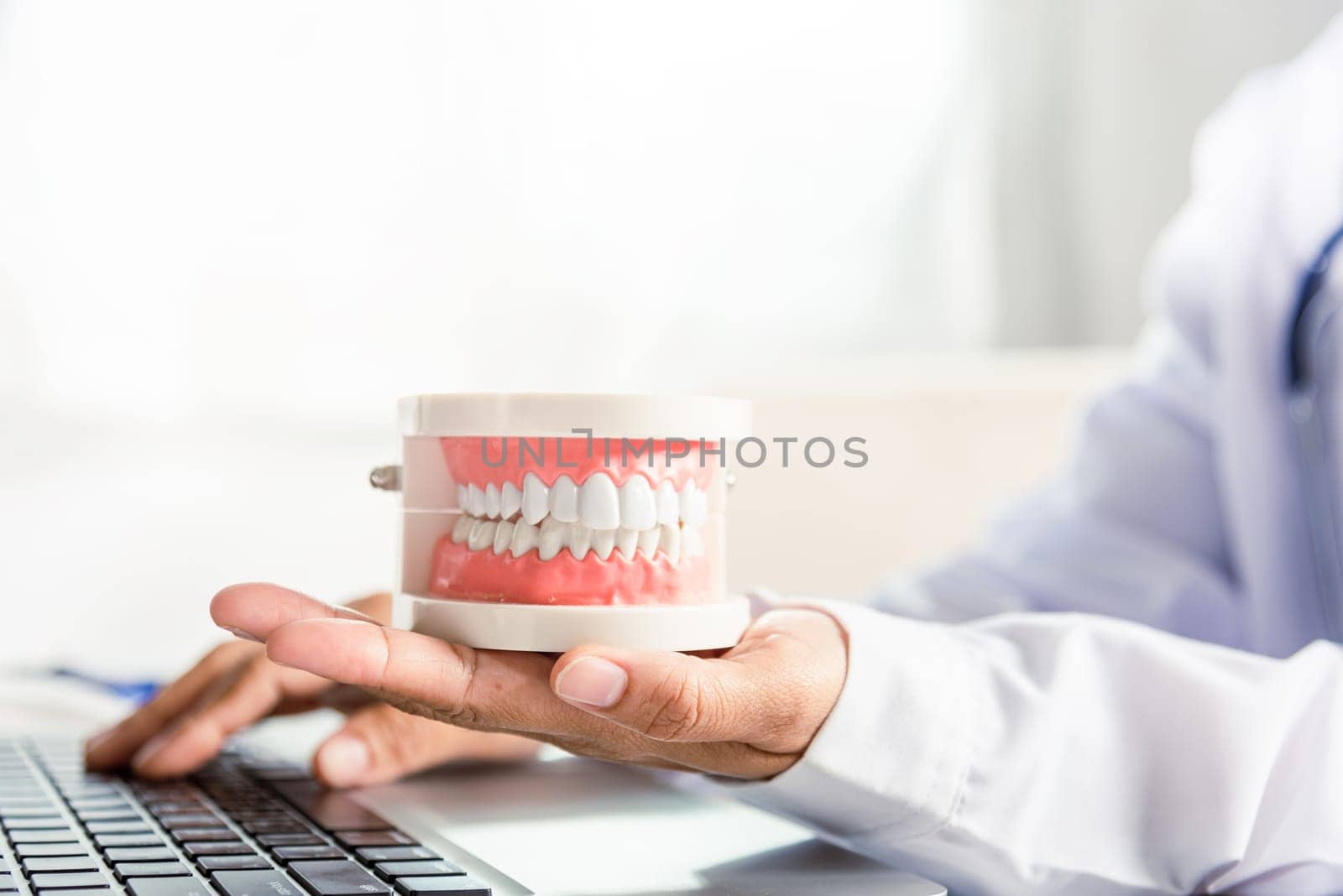 Female doctor sitting and hold tooth on desk at clinic office have laptop computer by Sorapop